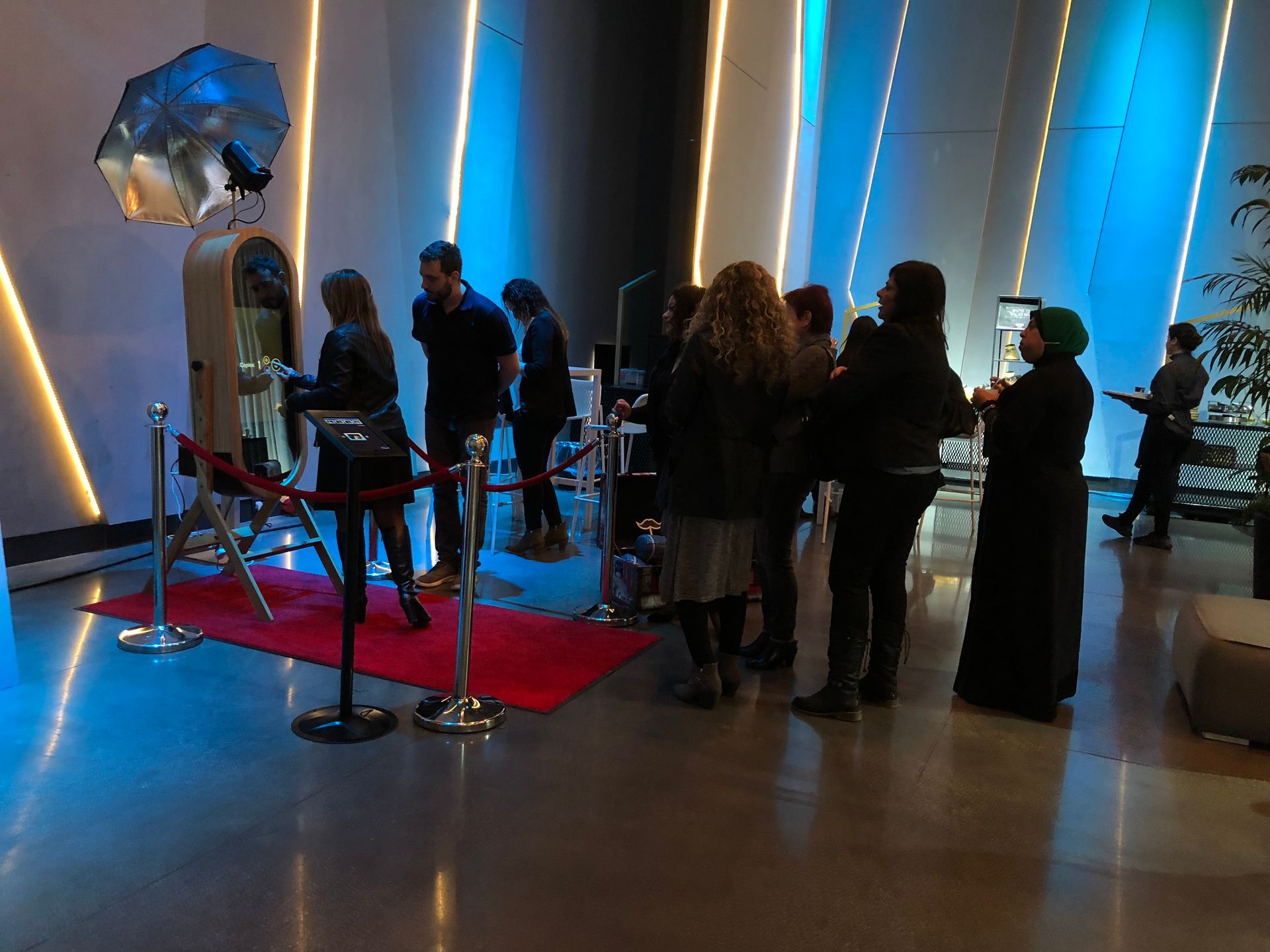 Guests gathered at a blue-lit event booth with a red carpet and metallic display