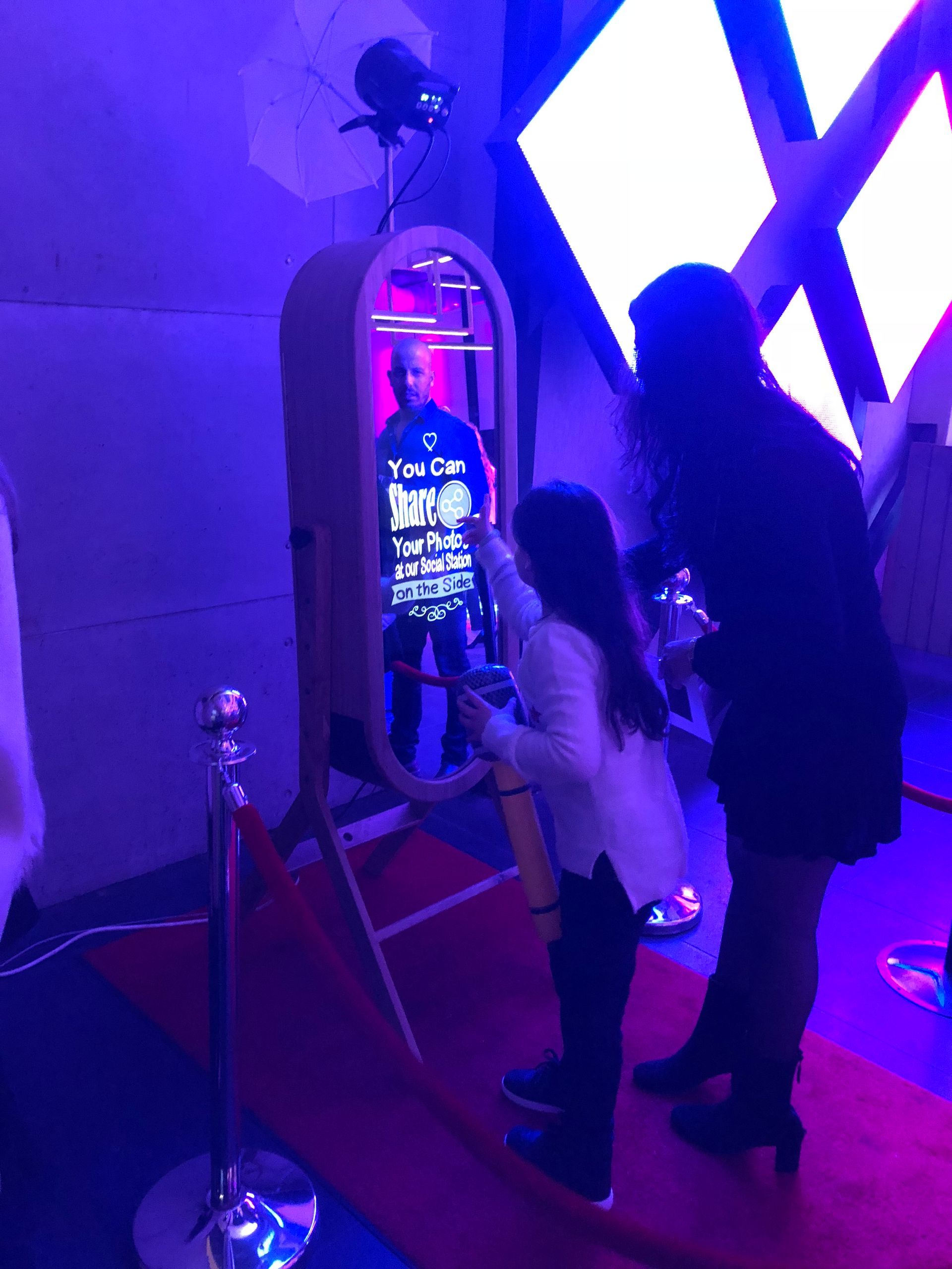 Two people using an interactive touchscreen mirror in a purple-lit room