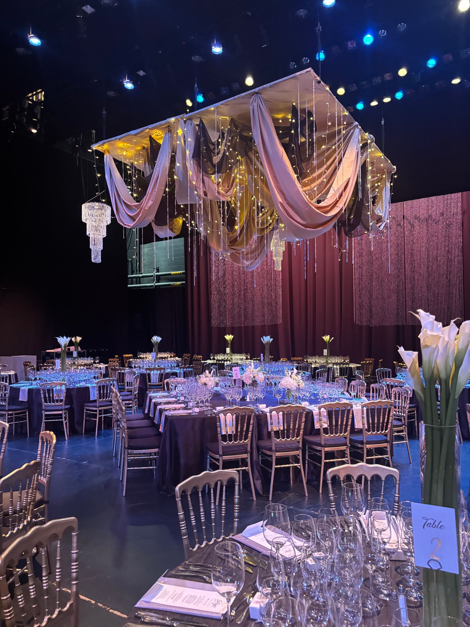 Elegant banquet hall with gold and lavender drapery, chandeliers, and set tables for an event