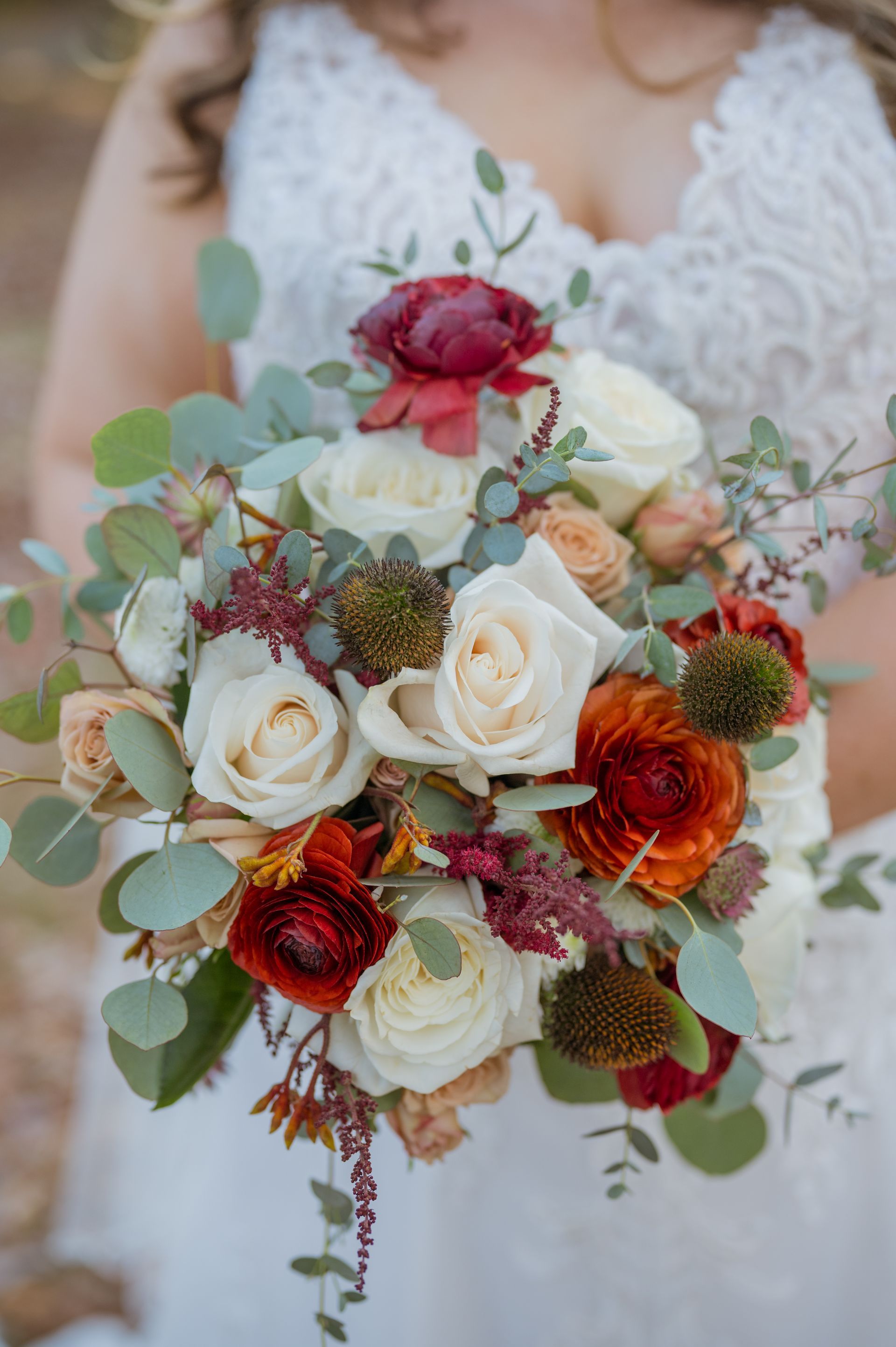 Bridal bouquet with white roses, burgundy flowers, and greenery held against a white lace dress