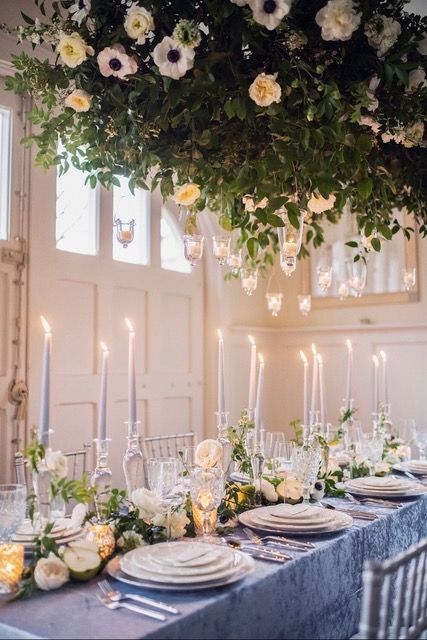 Elegant candlelit banquet table with blue runner, white dishes, and hanging floral greenery overhead