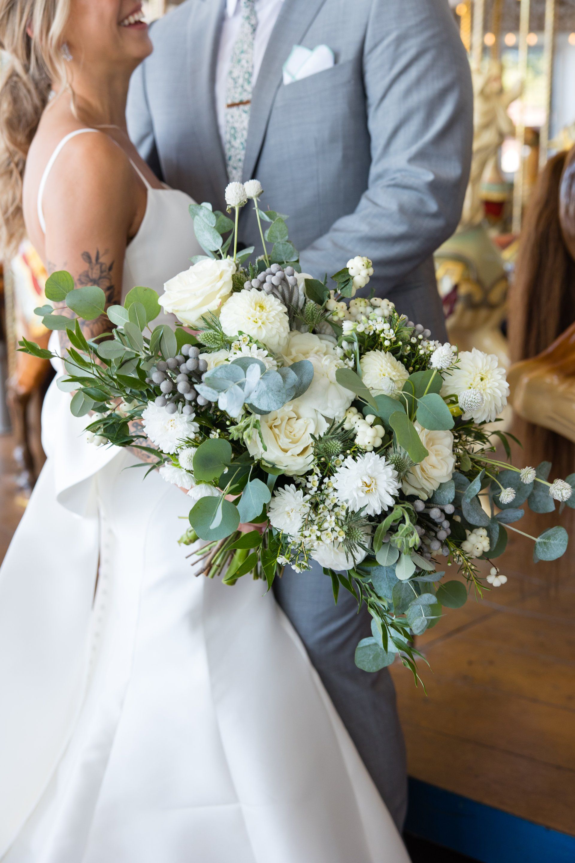 Bride holding a white and green bouquet beside a groom in a gray suit at an indoor wedding ceremony