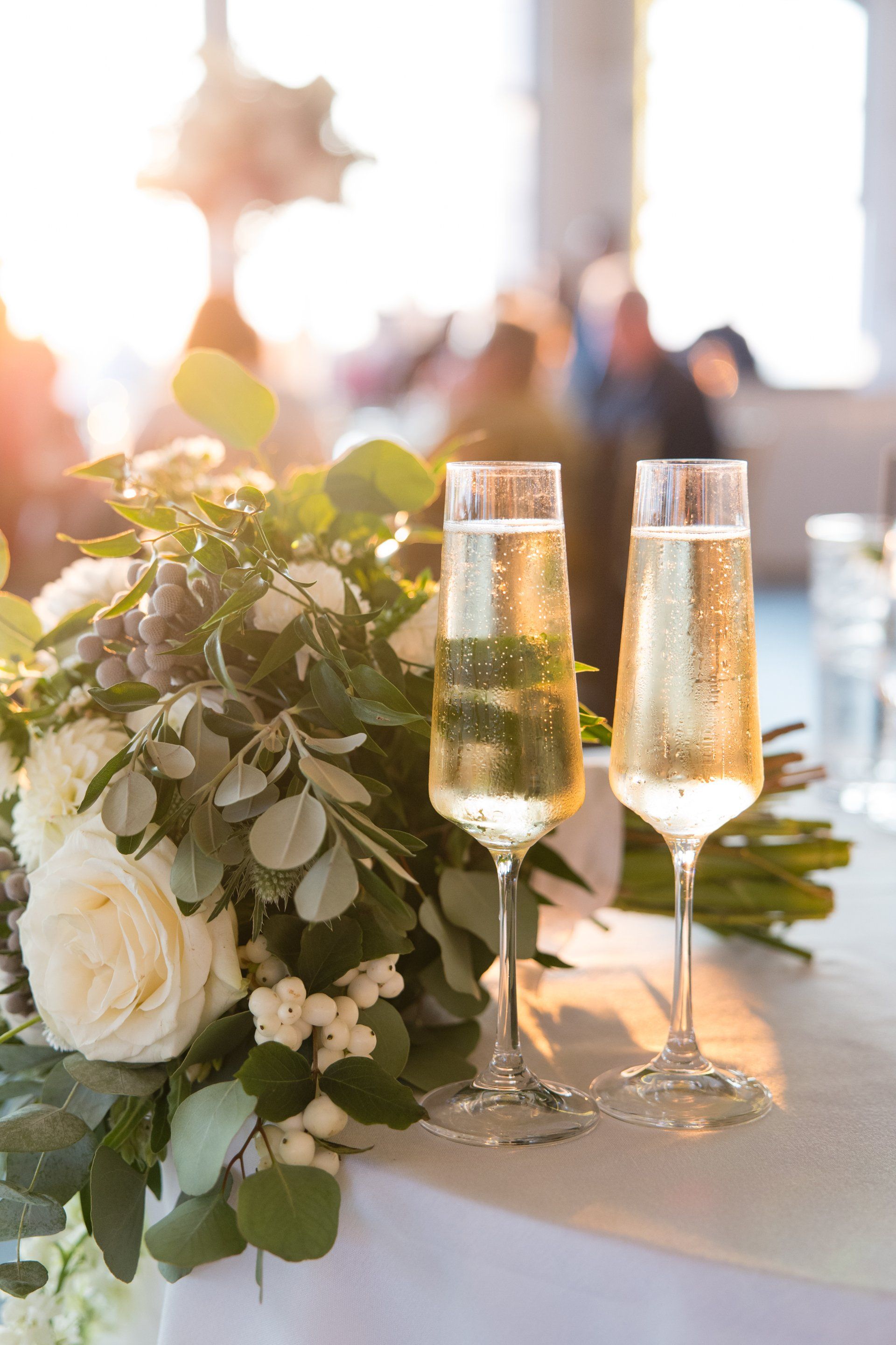 Champagne flutes beside a white floral centerpiece on a decorated reception table