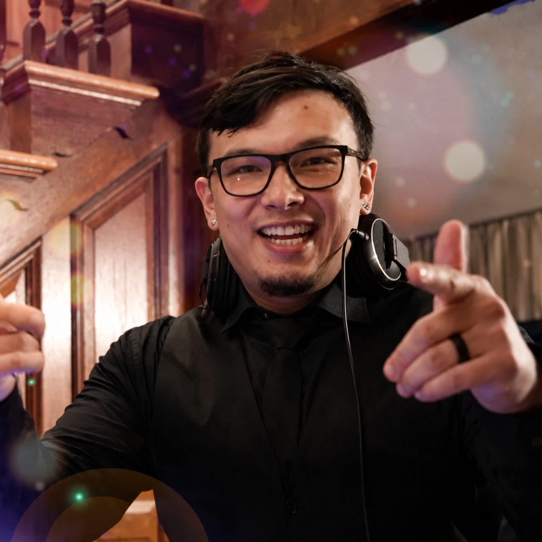 Person in glasses and black hoodie smiling and pointing at the camera in a warmly lit interior