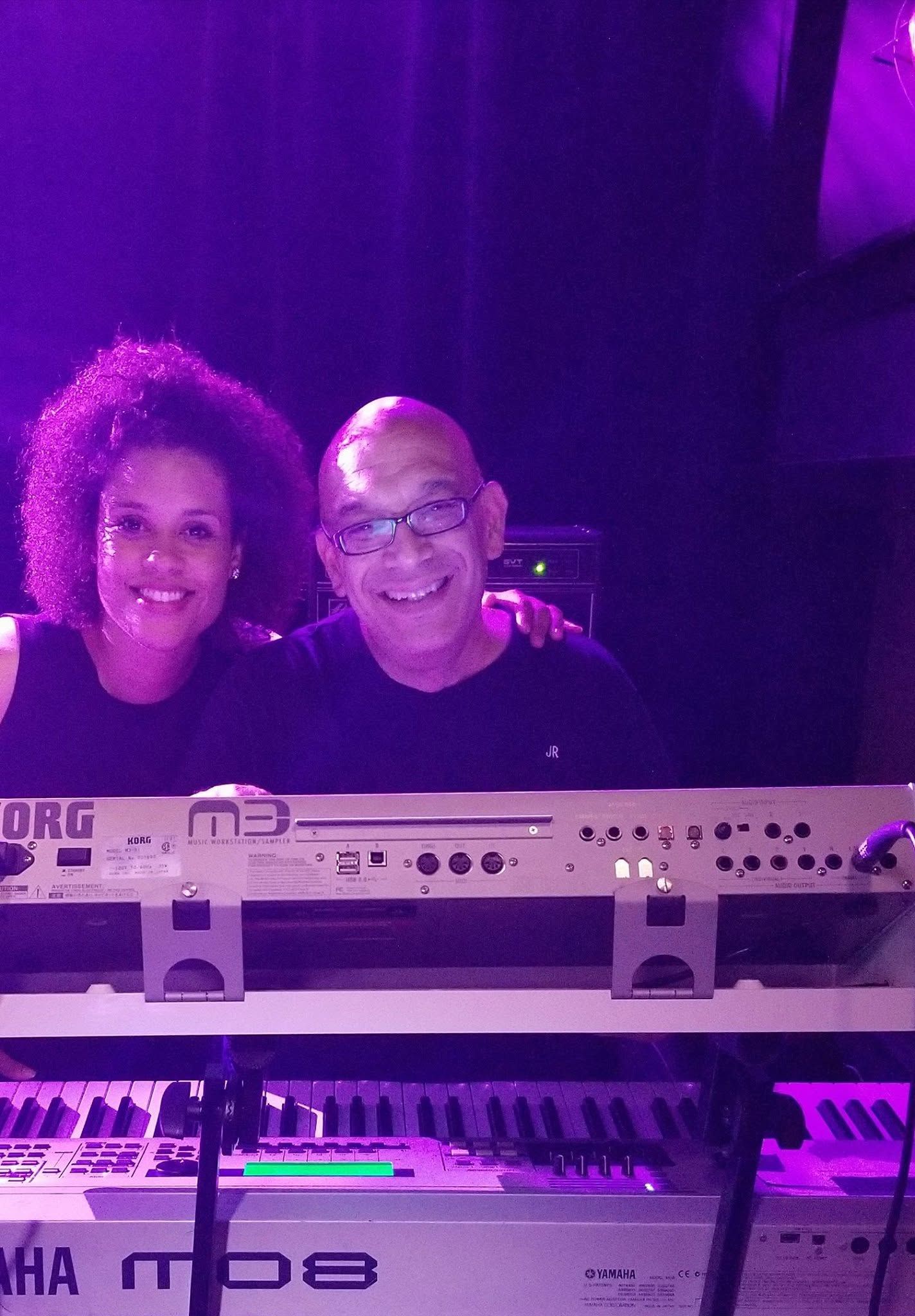 Two people smiling behind a keyboard on a purple-lit stage