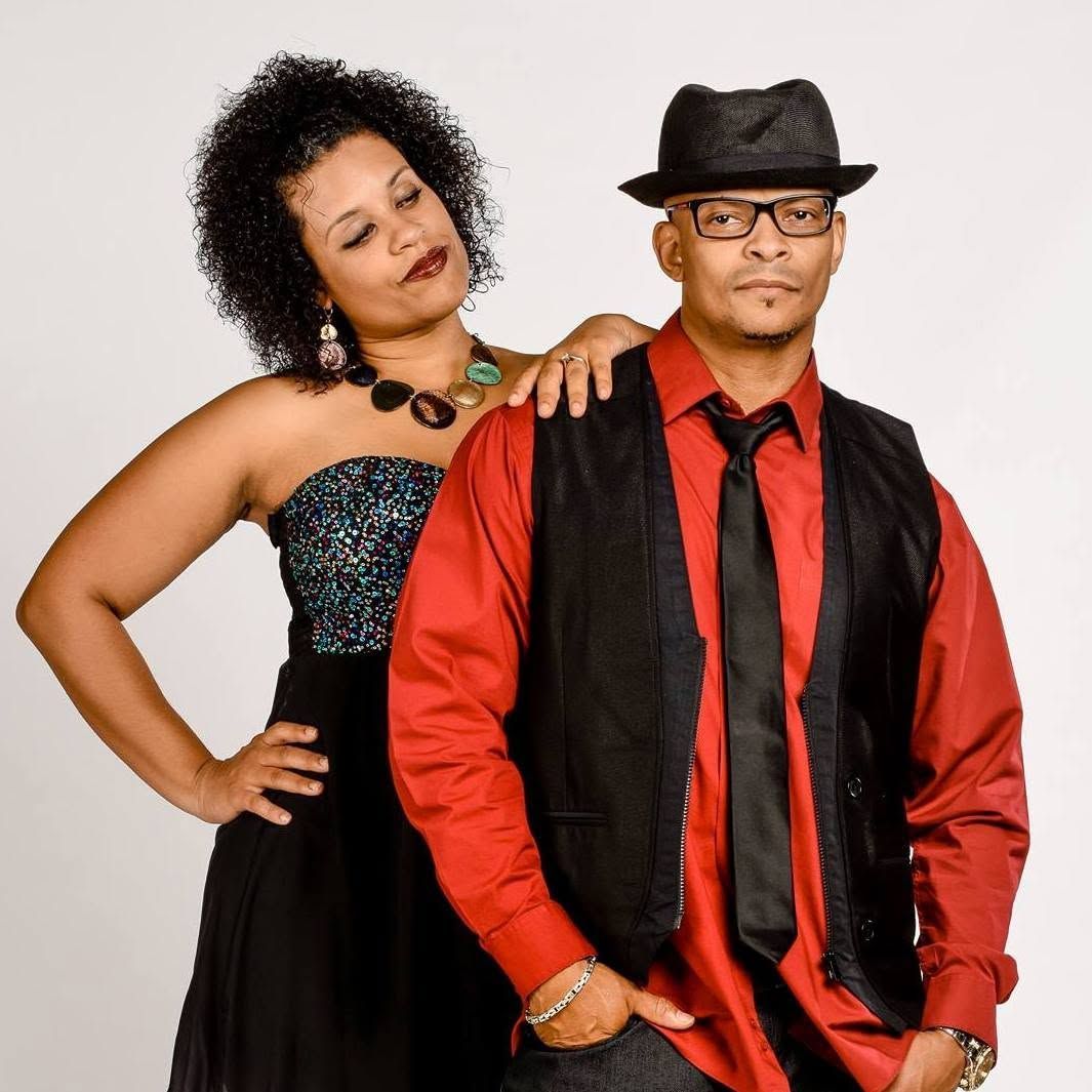 Two people posing in formal red and black outfits against a white background