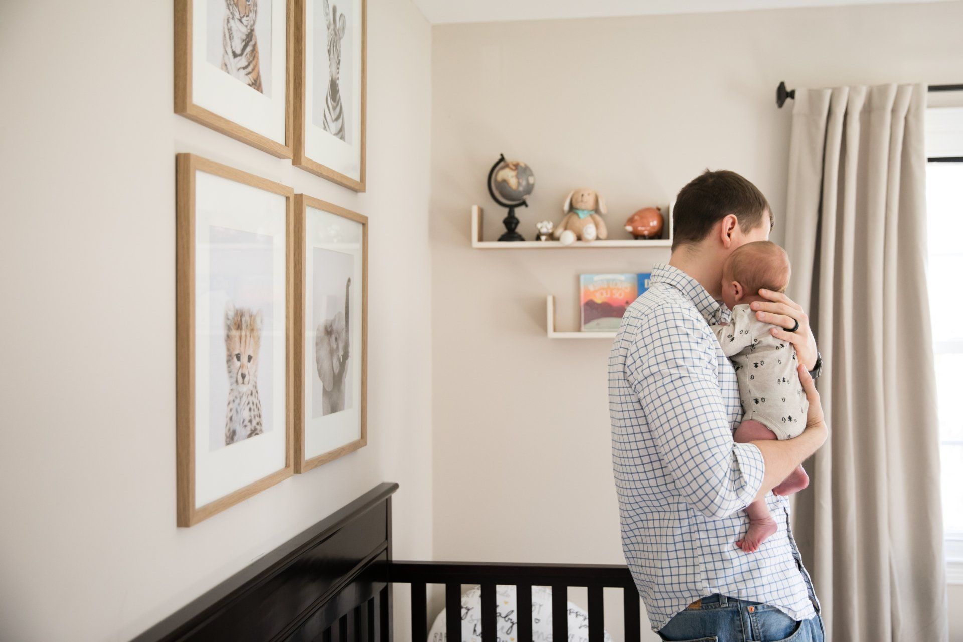 Father holding a baby in a nursery beside a crib and framed wall art