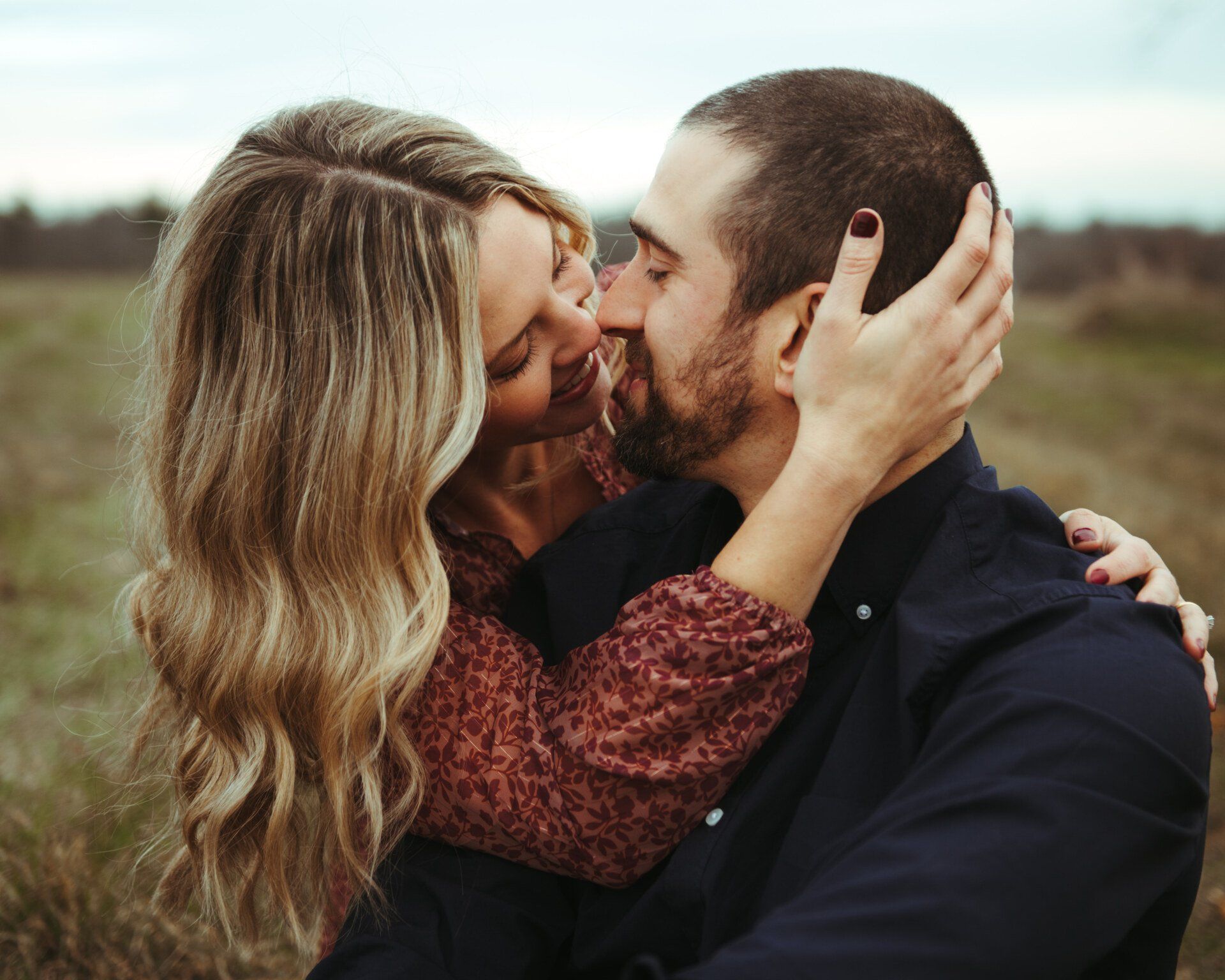 Couple embracing and kissing outdoors, with blurred grass field in the background.