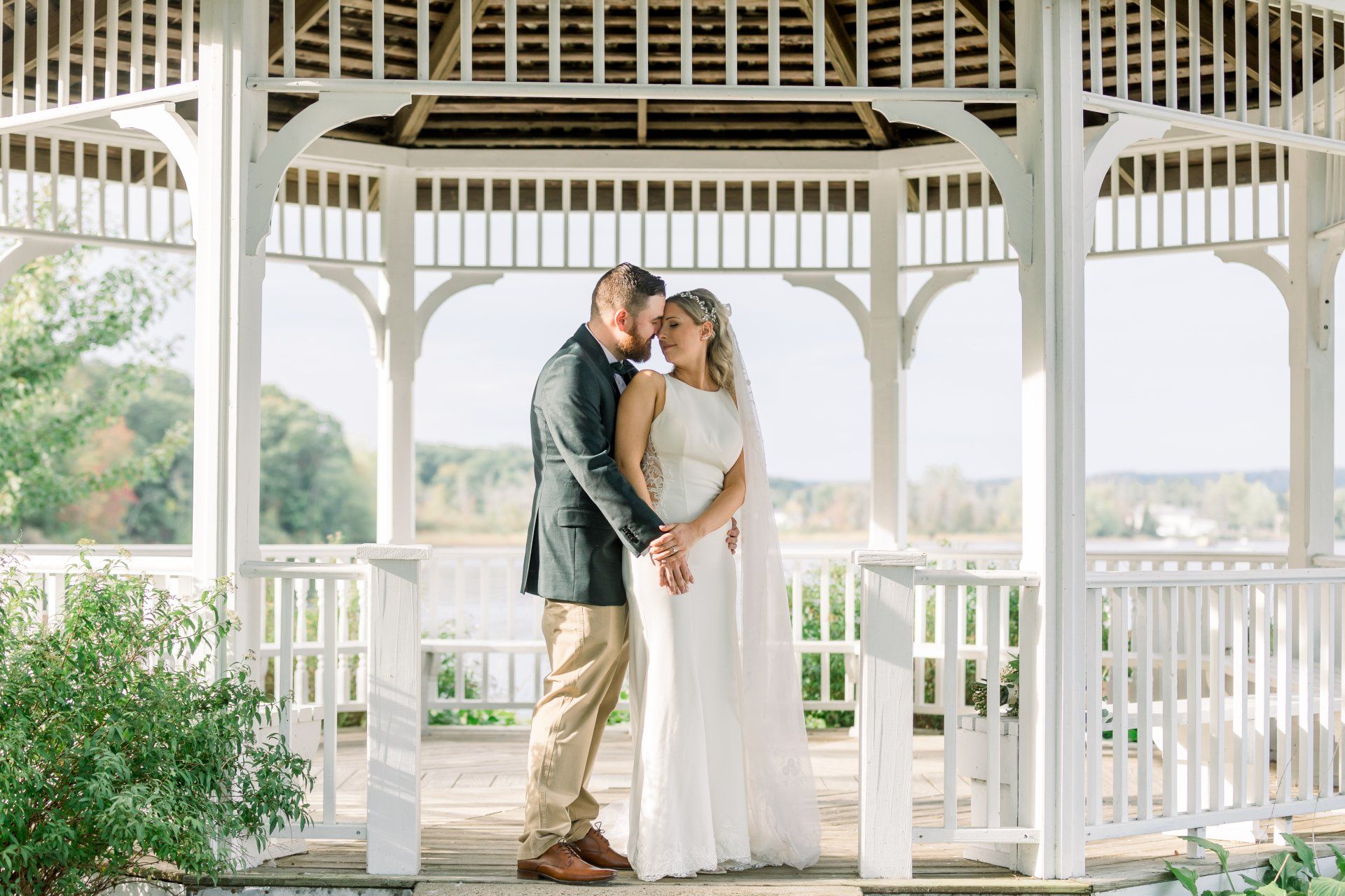 Couple embracing in a white gazebo, with the bride in a white dress and groom in a gray jacket.