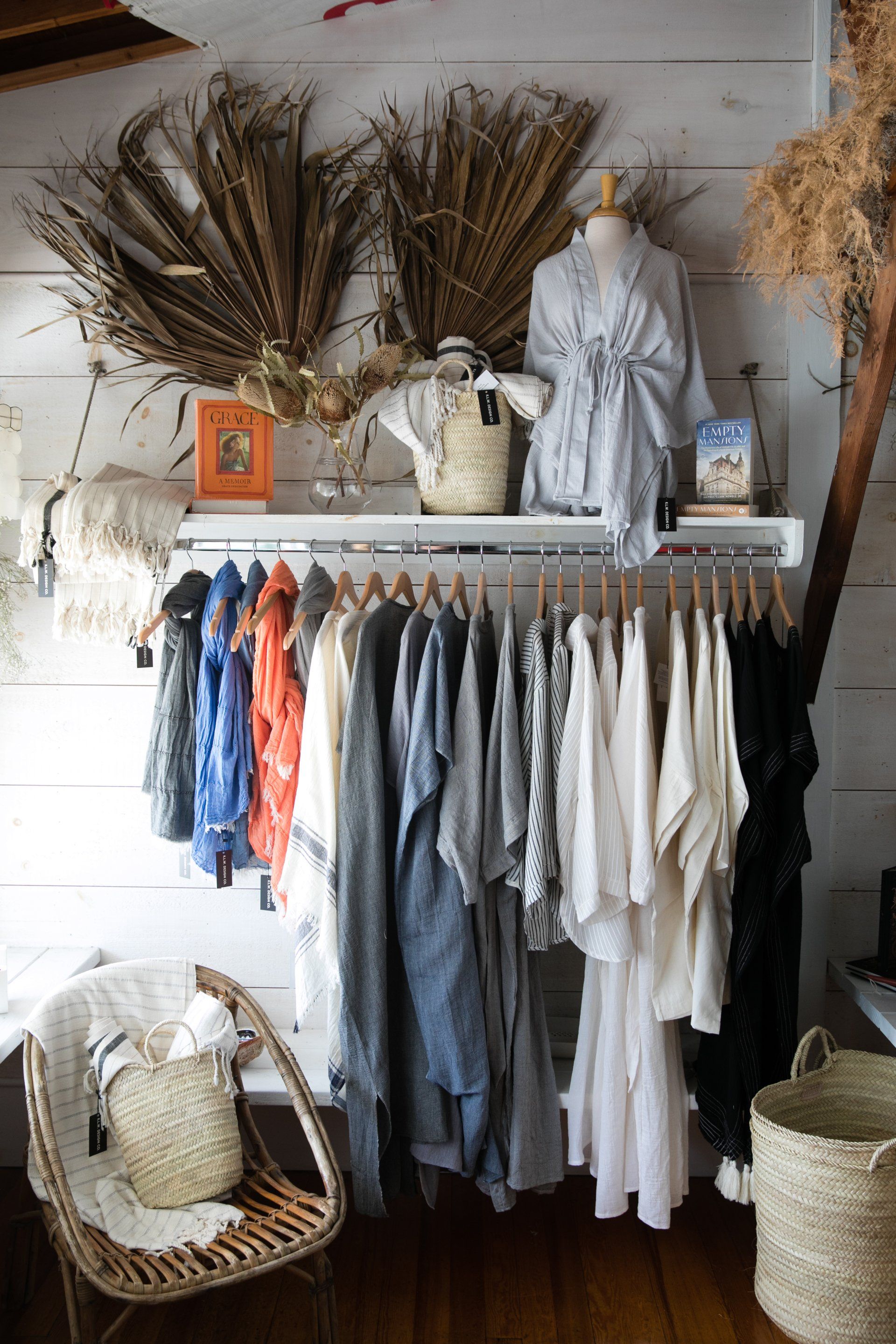 Boutique clothing rack with neutral garments, rustic decor, and woven baskets on a white wood wall