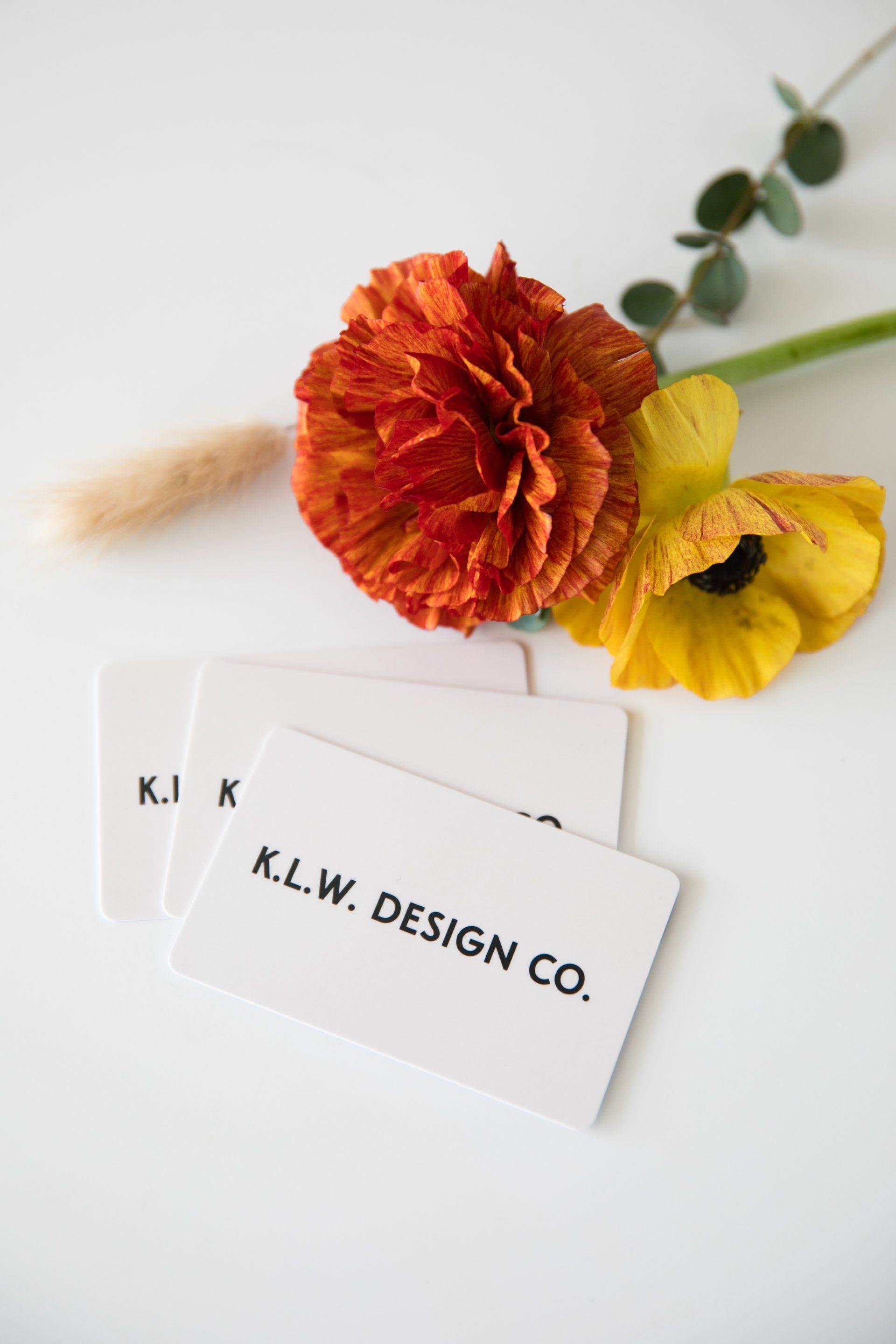 Business cards with K.L.W. DESIGN CO. beside orange and yellow flowers on a white background