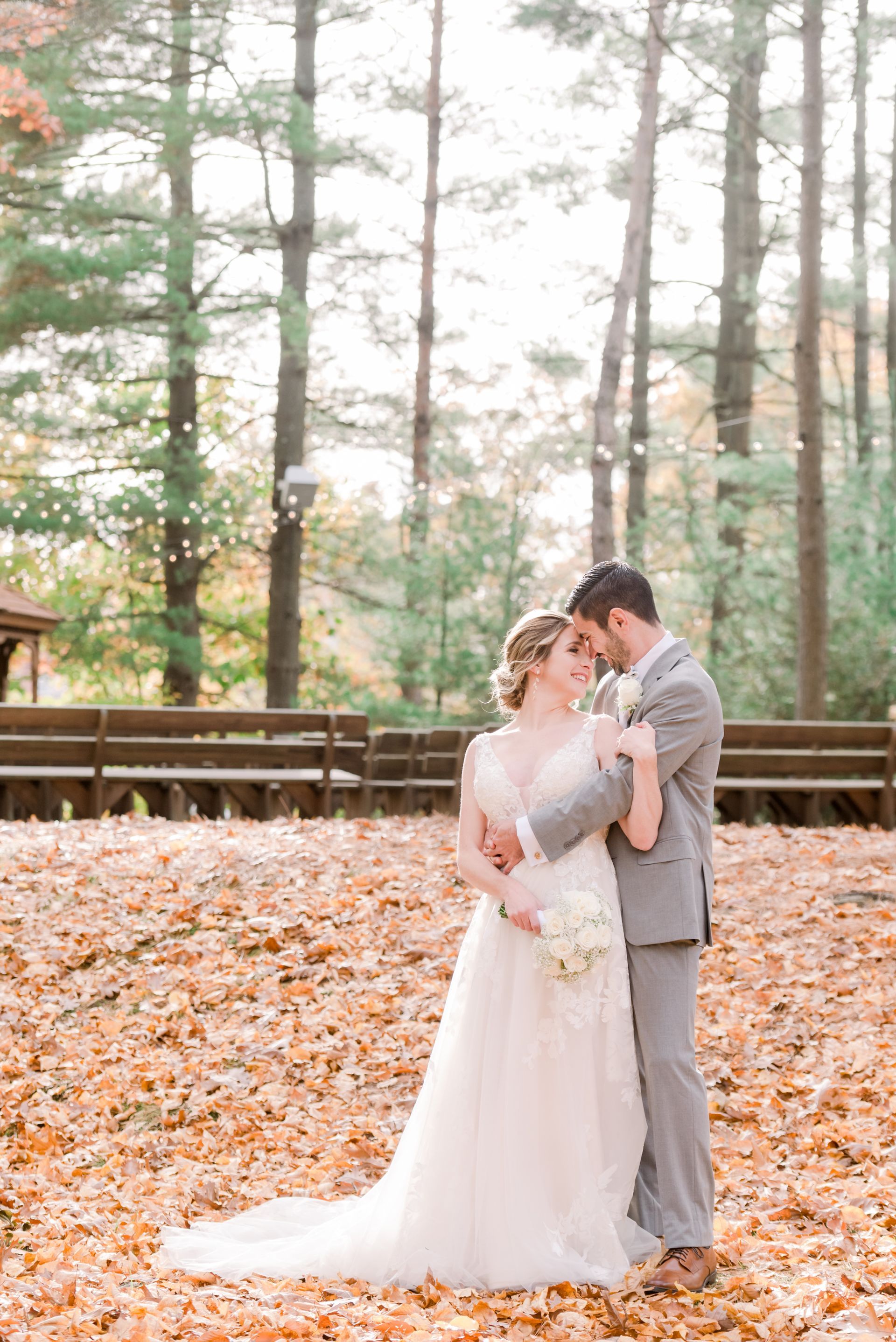 Bride and groom embracing in a forest with autumn leaves and tall trees