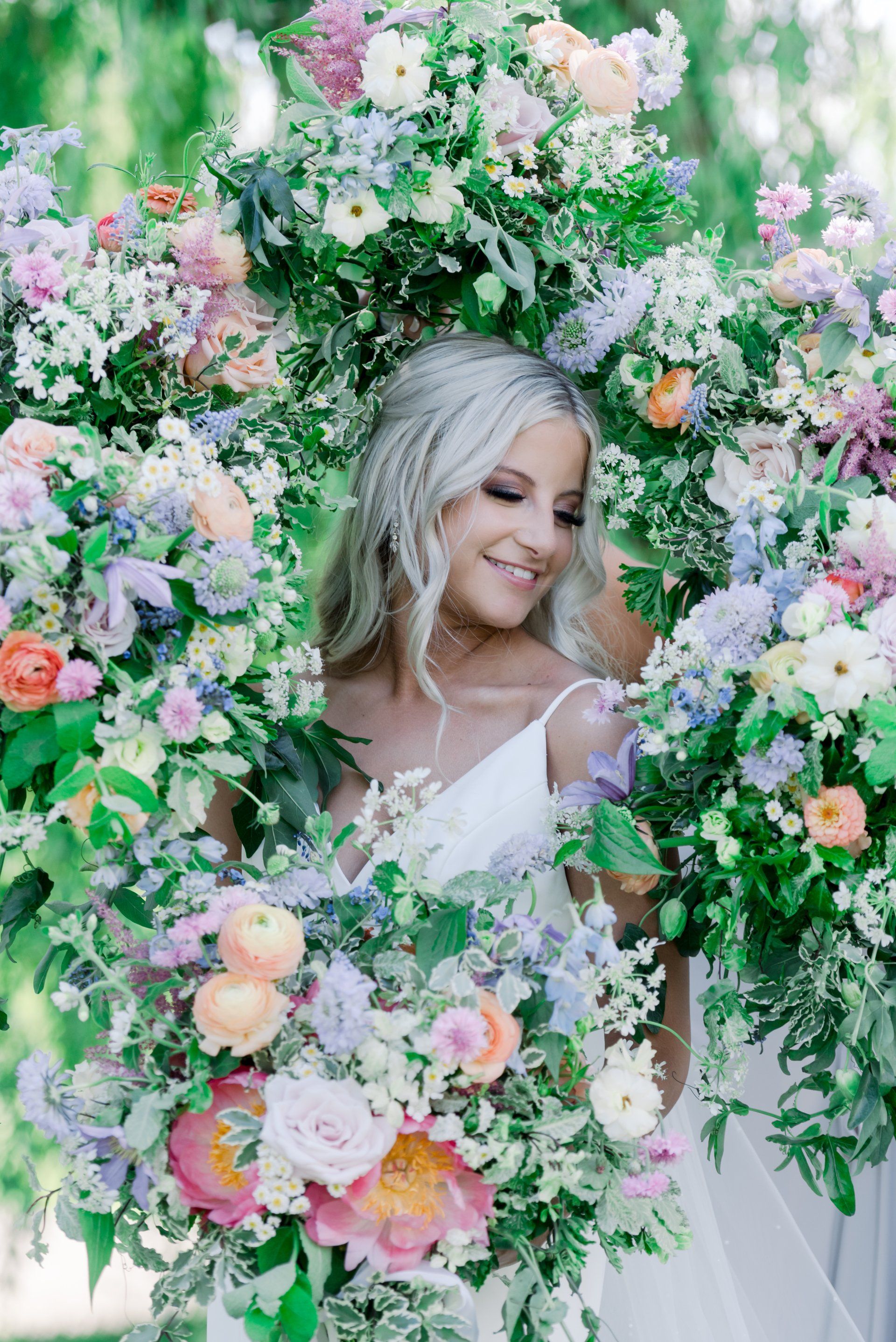 Smiling woman in a white dress surrounded by lush pastel flowers and greenery