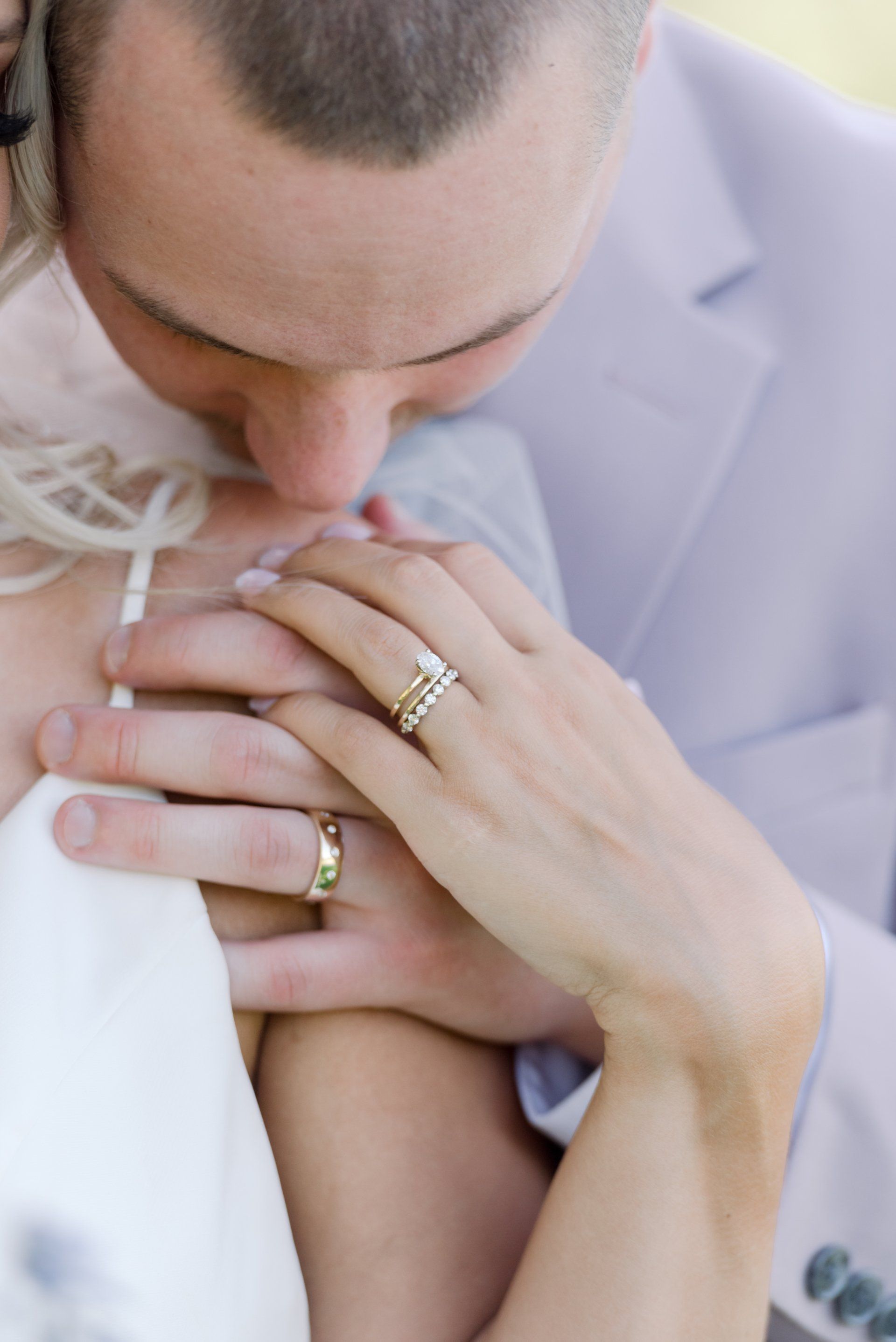 Close-up of a couple embracing, with hands and wedding rings visible against a light suit.
