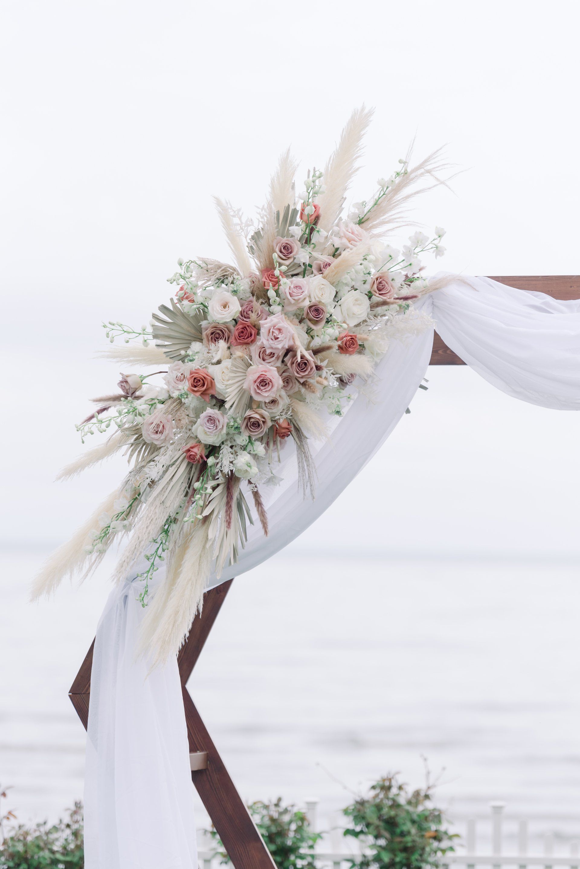 Floral wedding arch with white drapery and blush flowers overlooking the sea