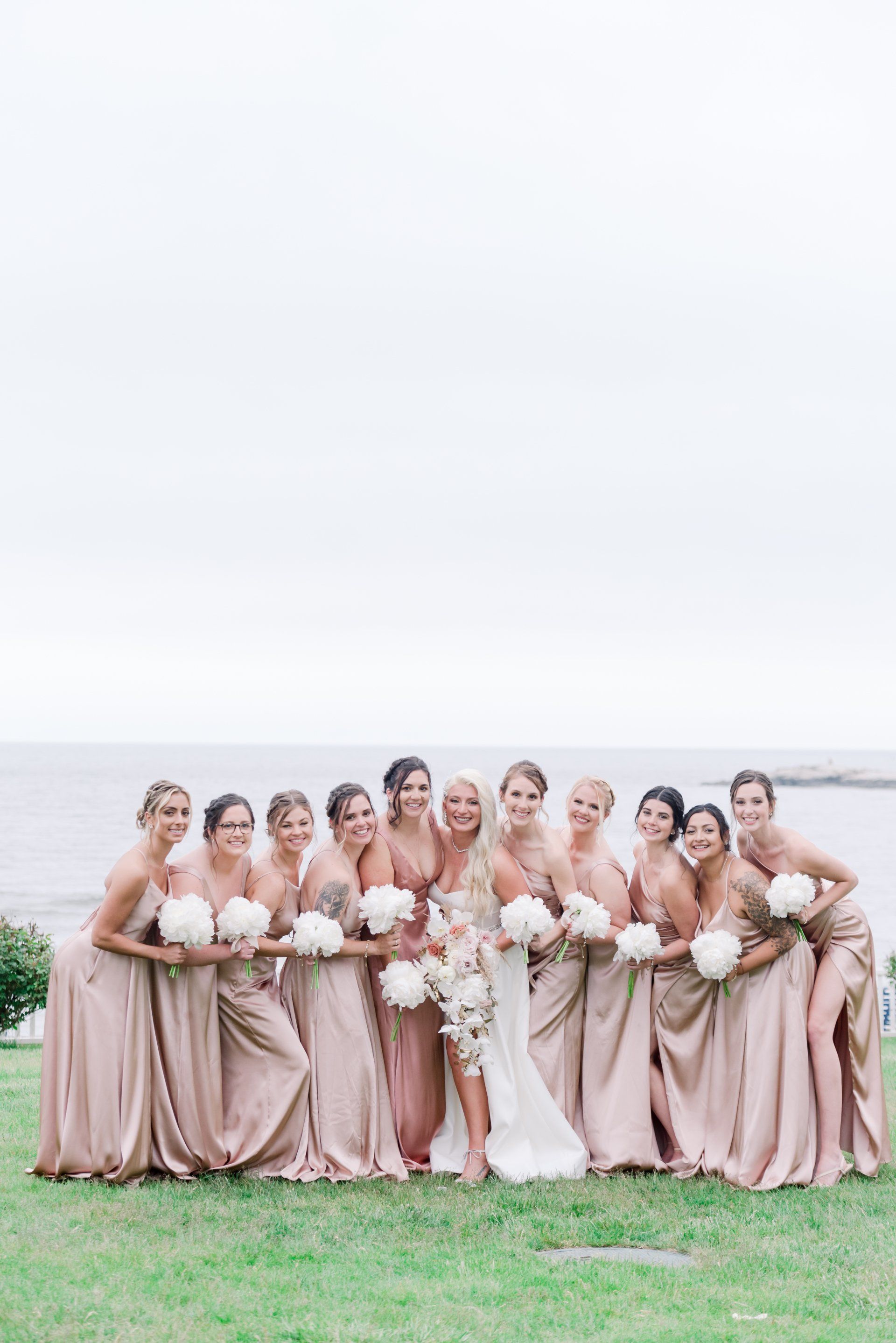 Bridal party in blush dresses holding bouquets with bride in white by the water