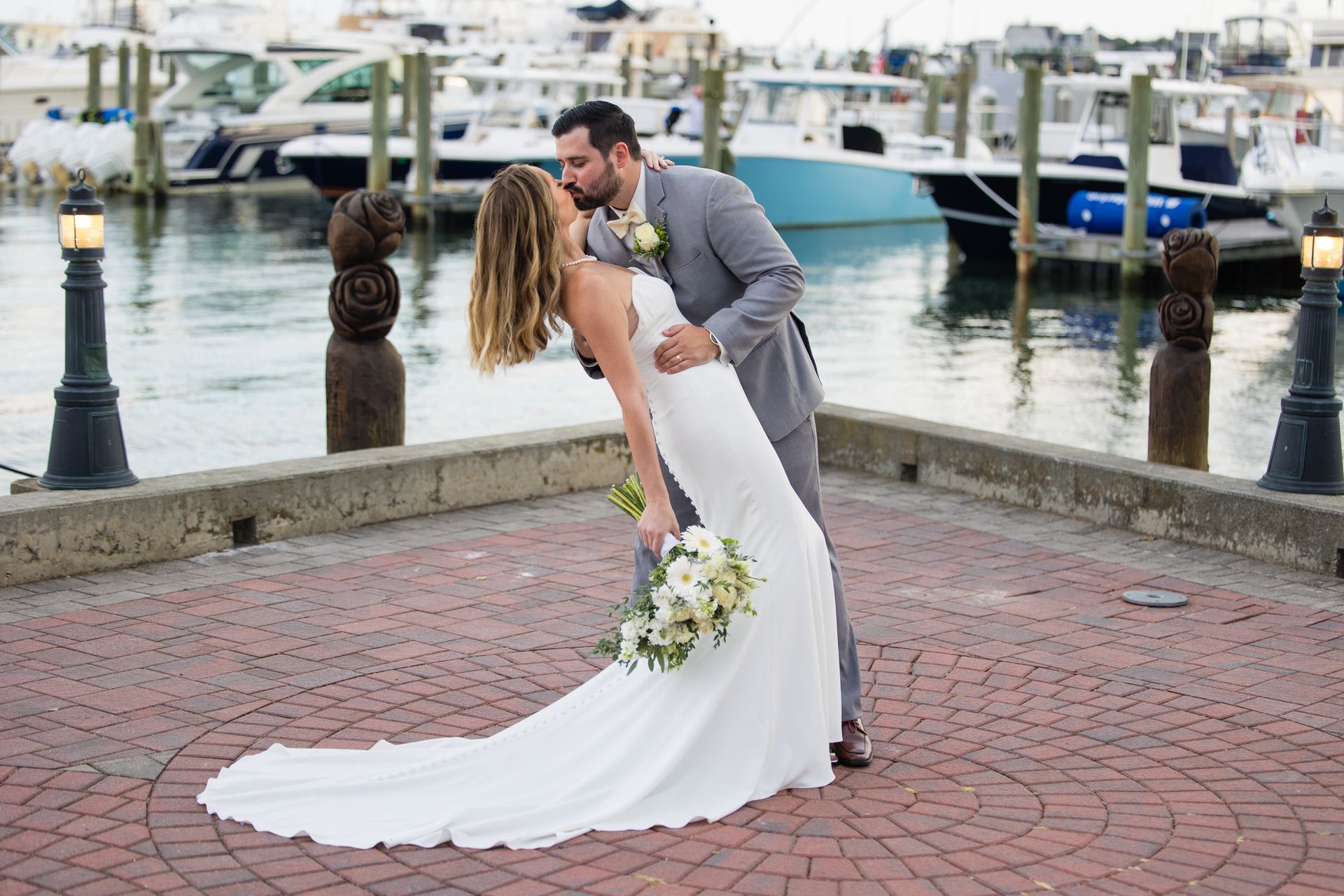 Bride and groom kissing at a waterfront dock, with boats in the background.