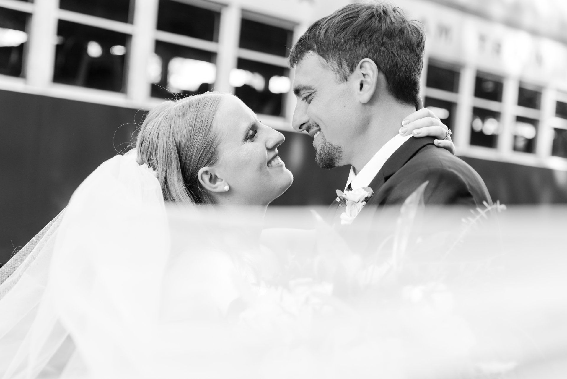 Smiling bride and groom gazing at each other, with veil flowing in a black-and-white close-up.