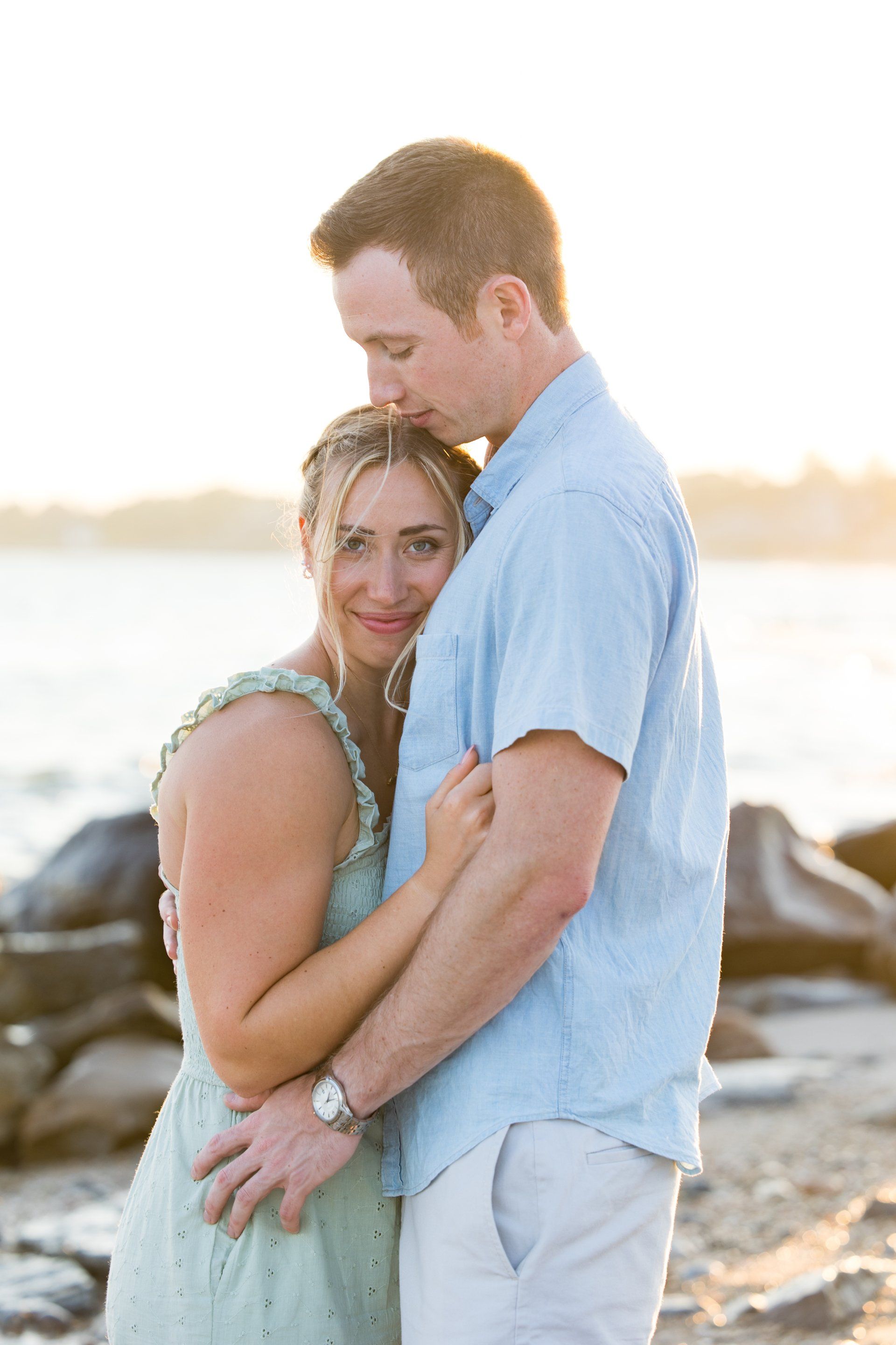Couple embracing on a rocky beach at sunset, with calm water in the background