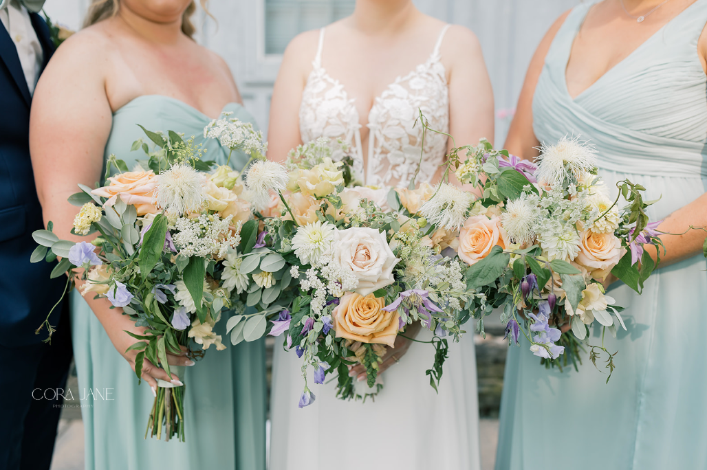 Three bridesmaids in pastel dresses holding white and peach floral bouquets
