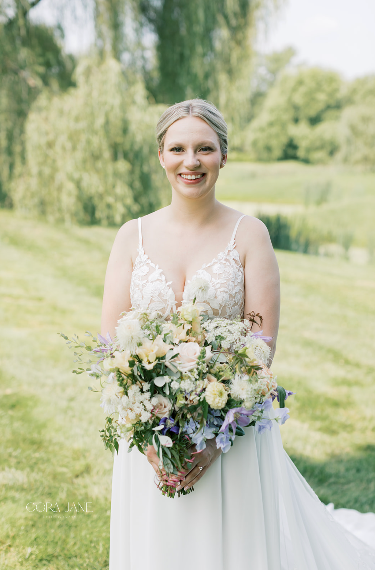 Bride in a white gown holding a pastel bouquet outdoors, smiling in a sunny garden