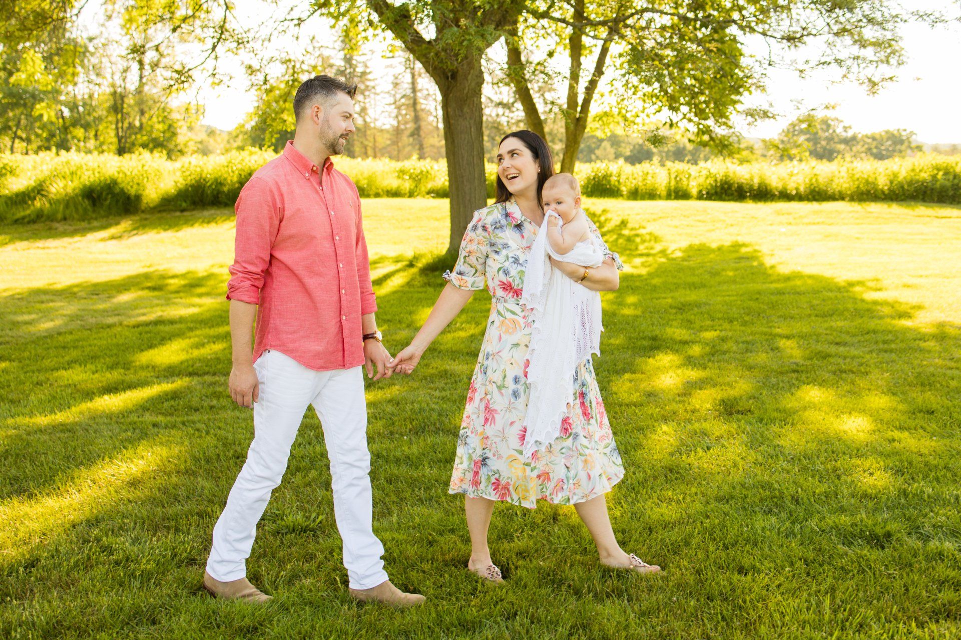 Two people holding hands and smiling in a sunny grassy park, with trees in the background