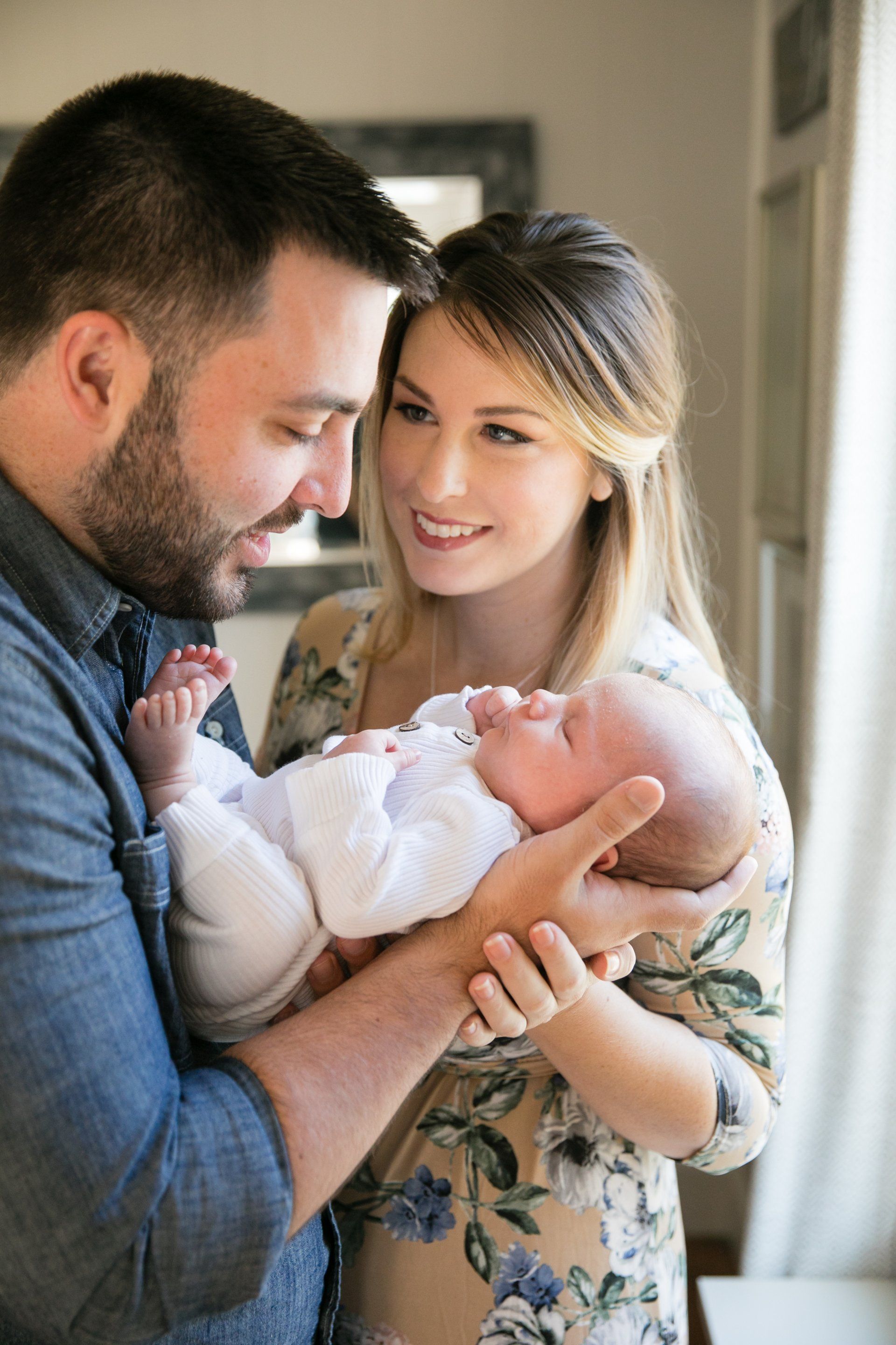 Couple gently holding a sleeping newborn near a window