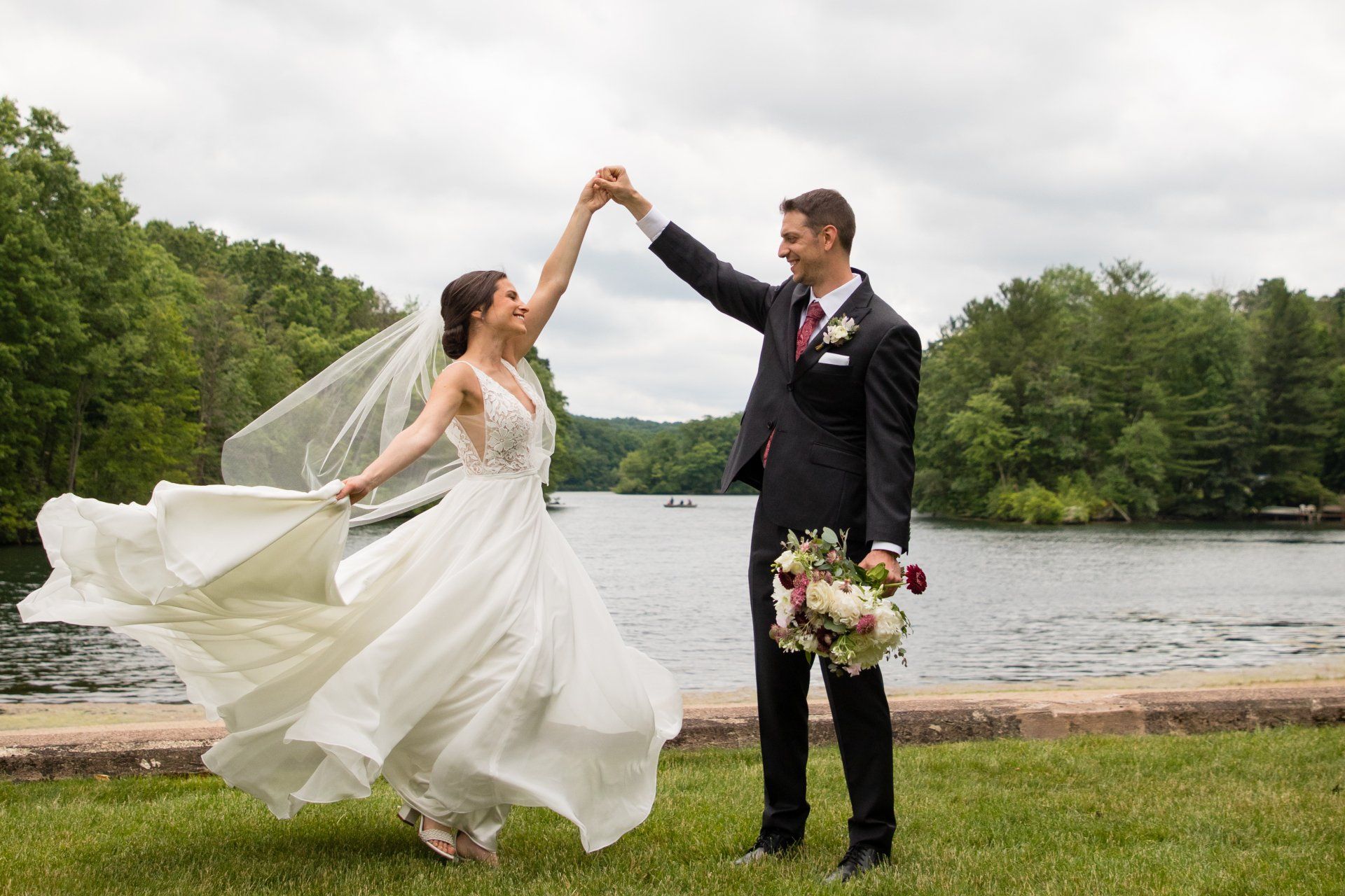 Bride and groom dancing by a lakeside, with the bride's dress and veil flowing in the wind