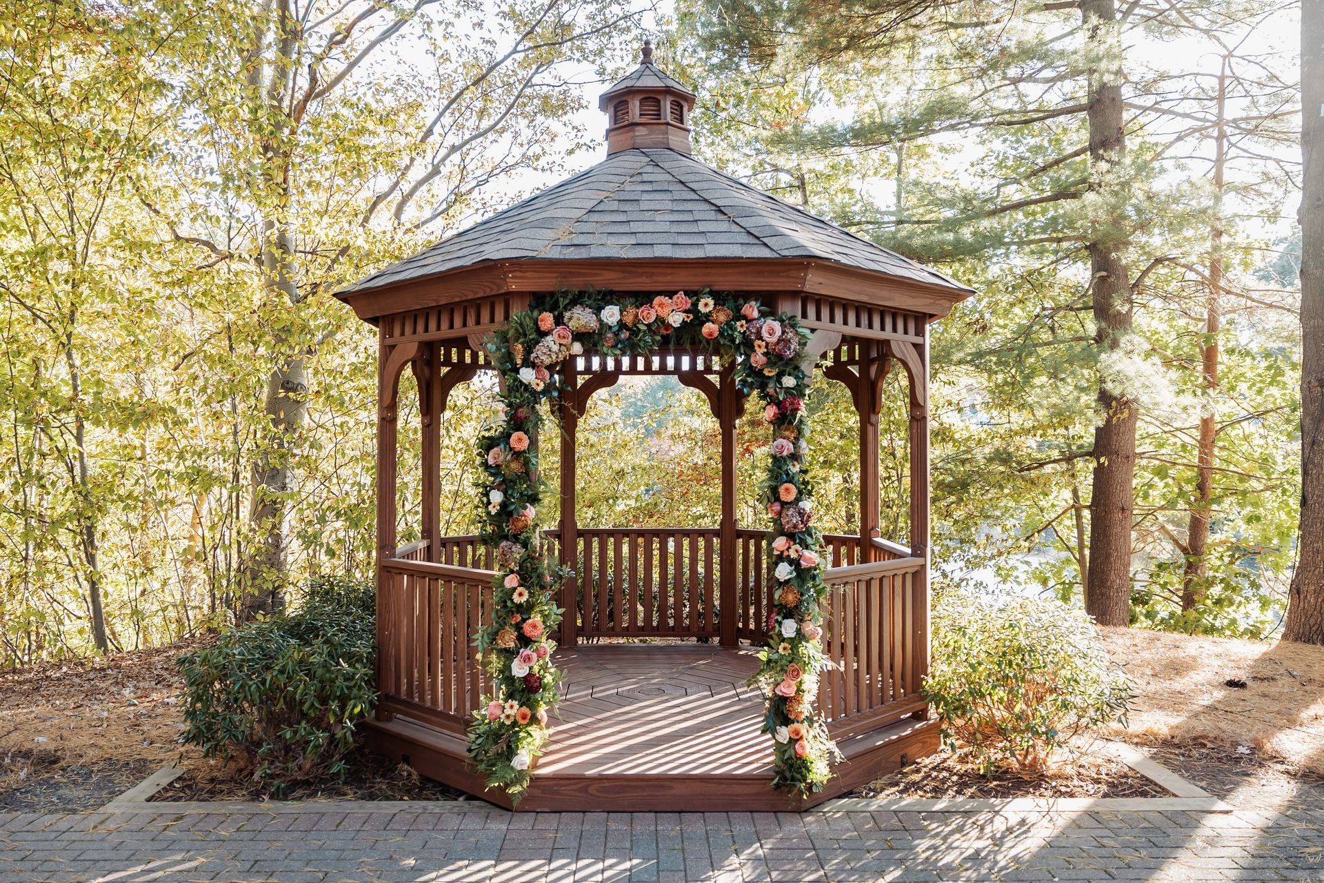 Wooden gazebo decorated with flowers in a sunlit wooded park