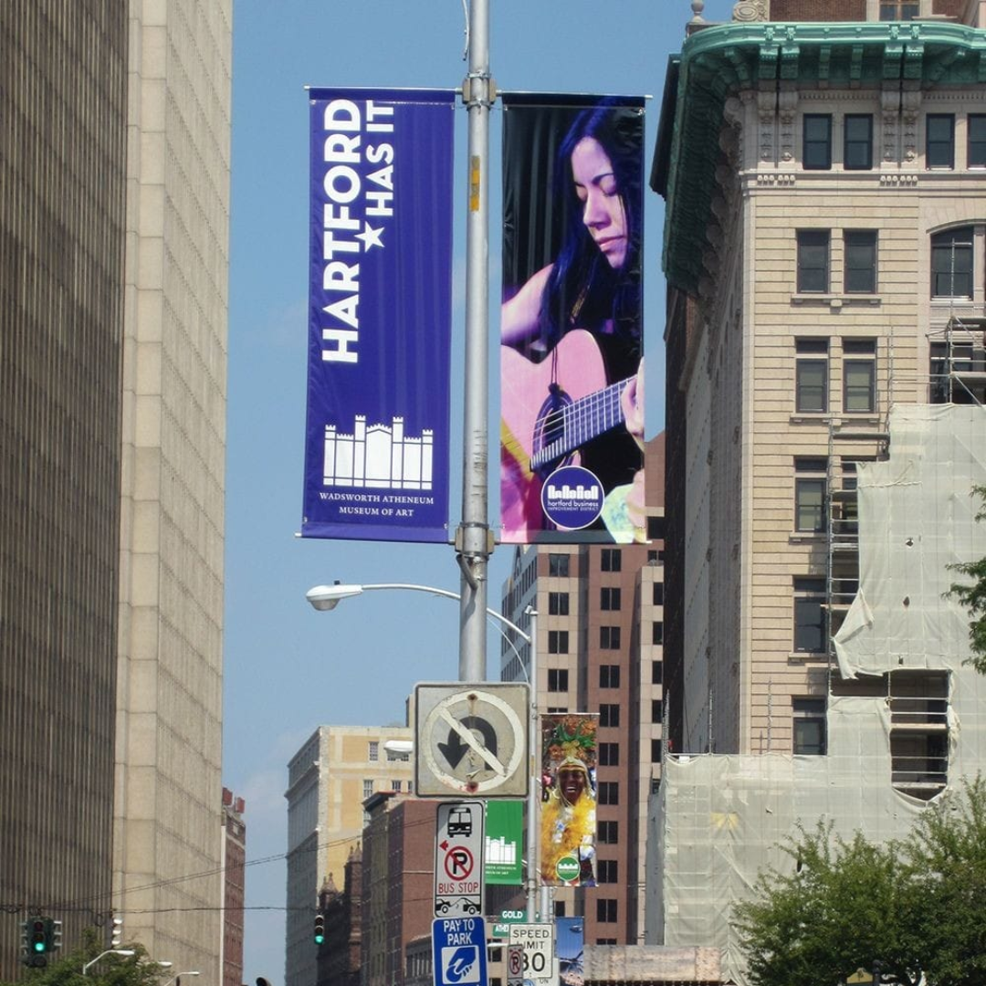 Downtown street with a Hartford banner and a large vertical ad showing a musician playing guitar.