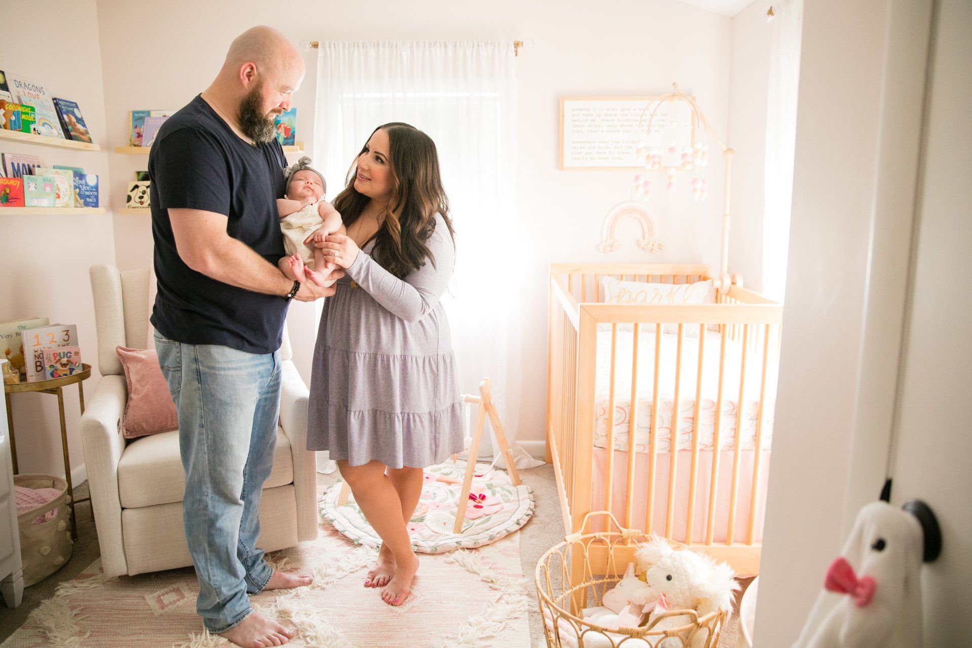 Couple holding a baby in a bright nursery beside a crib and soft toys