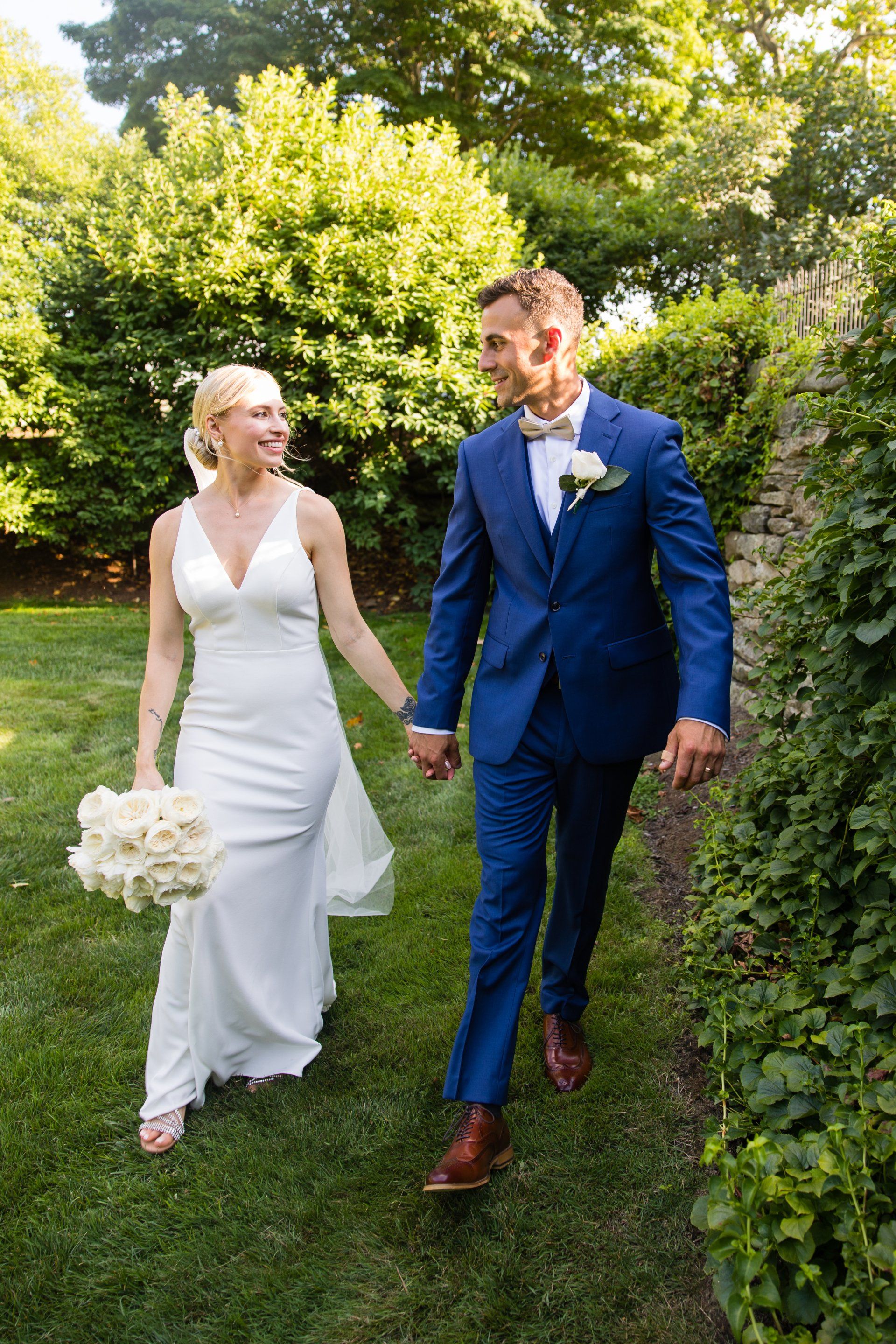 Bride and groom walking hand in hand outdoors in a garden, both in formal wedding attire