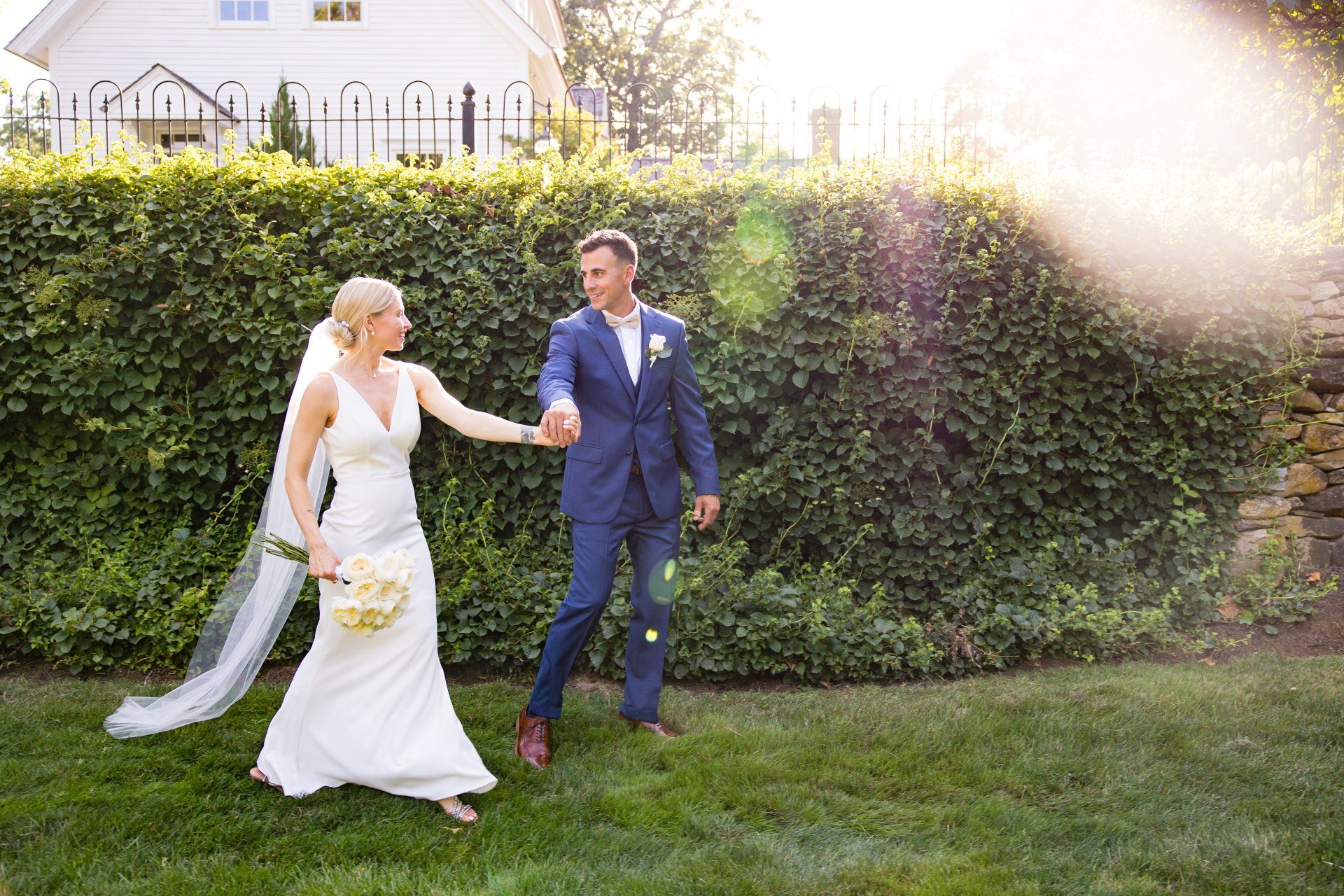 Bride and groom holding hands and walking on grass in a sunlit garden