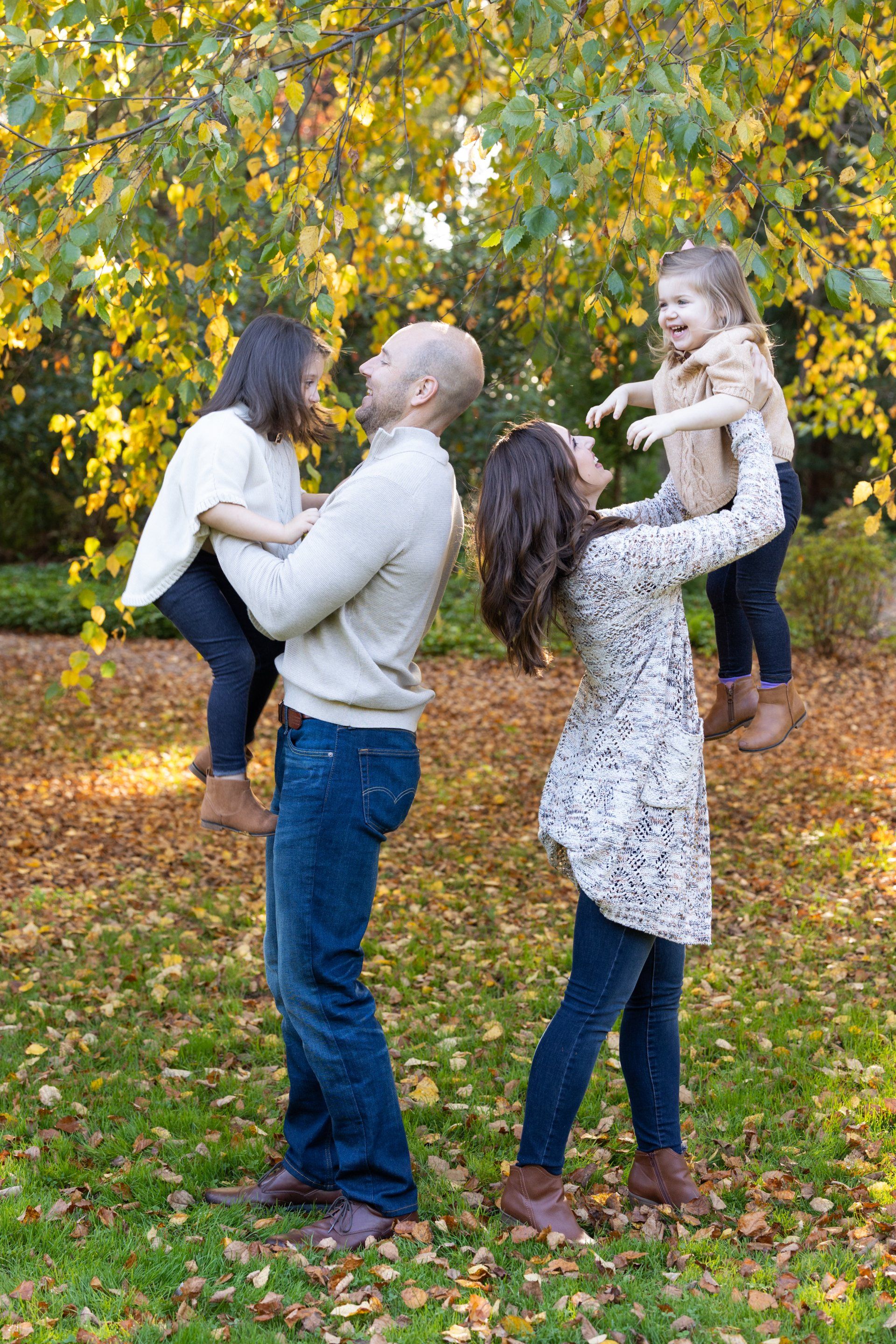 Two adults hold two smiling children in a leafy autumn park