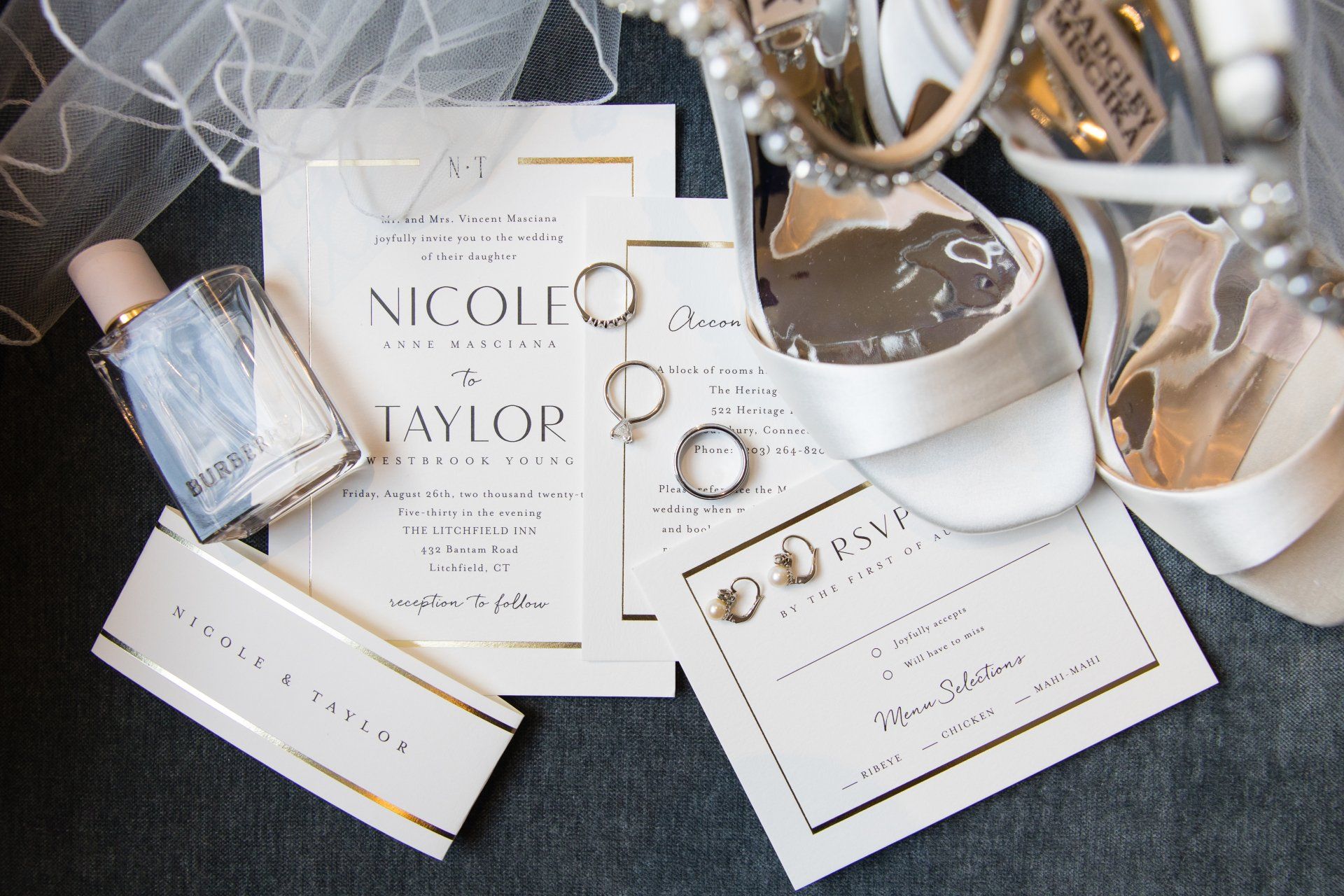 Elegant wedding stationery with rings, invitations, ribbon, and a white box on a dark surface