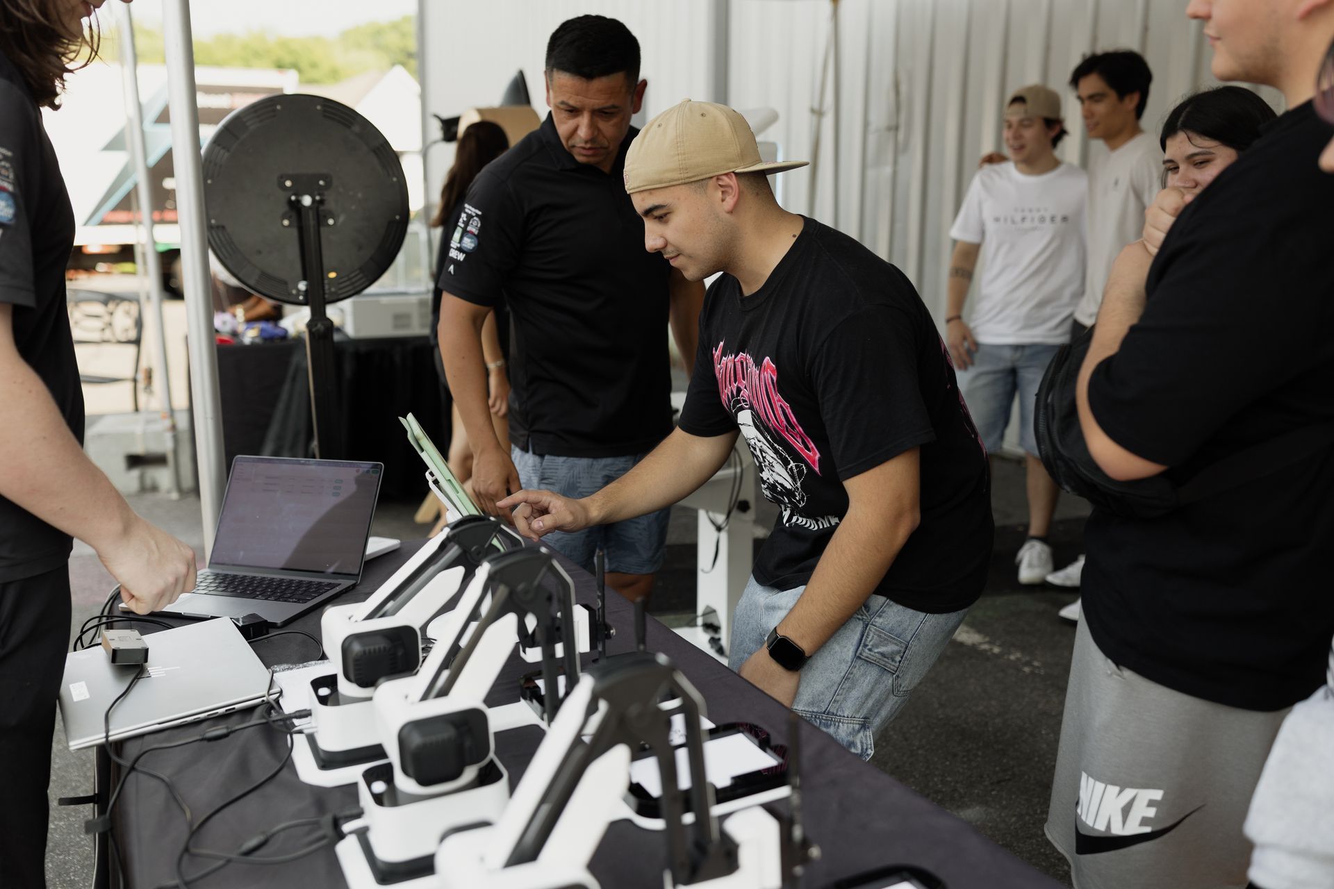 People examining drone parts and equipment on a table at an indoor tech demo booth