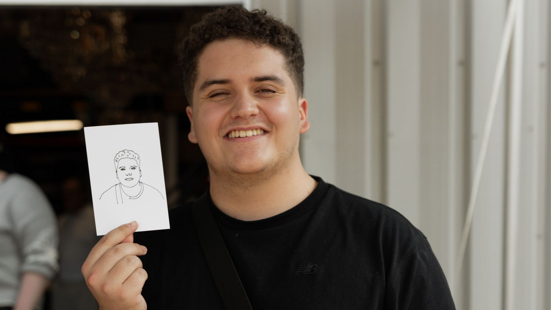 Smiling person holding a small sketch on white paper indoors