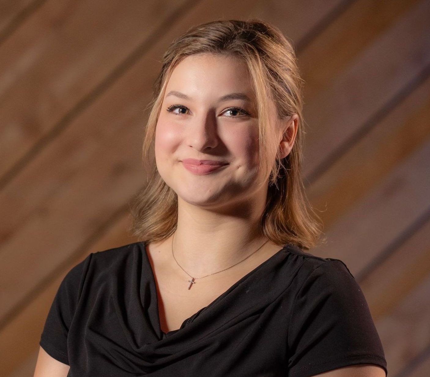 Smiling person in a black top against a warm wood-paneled background
