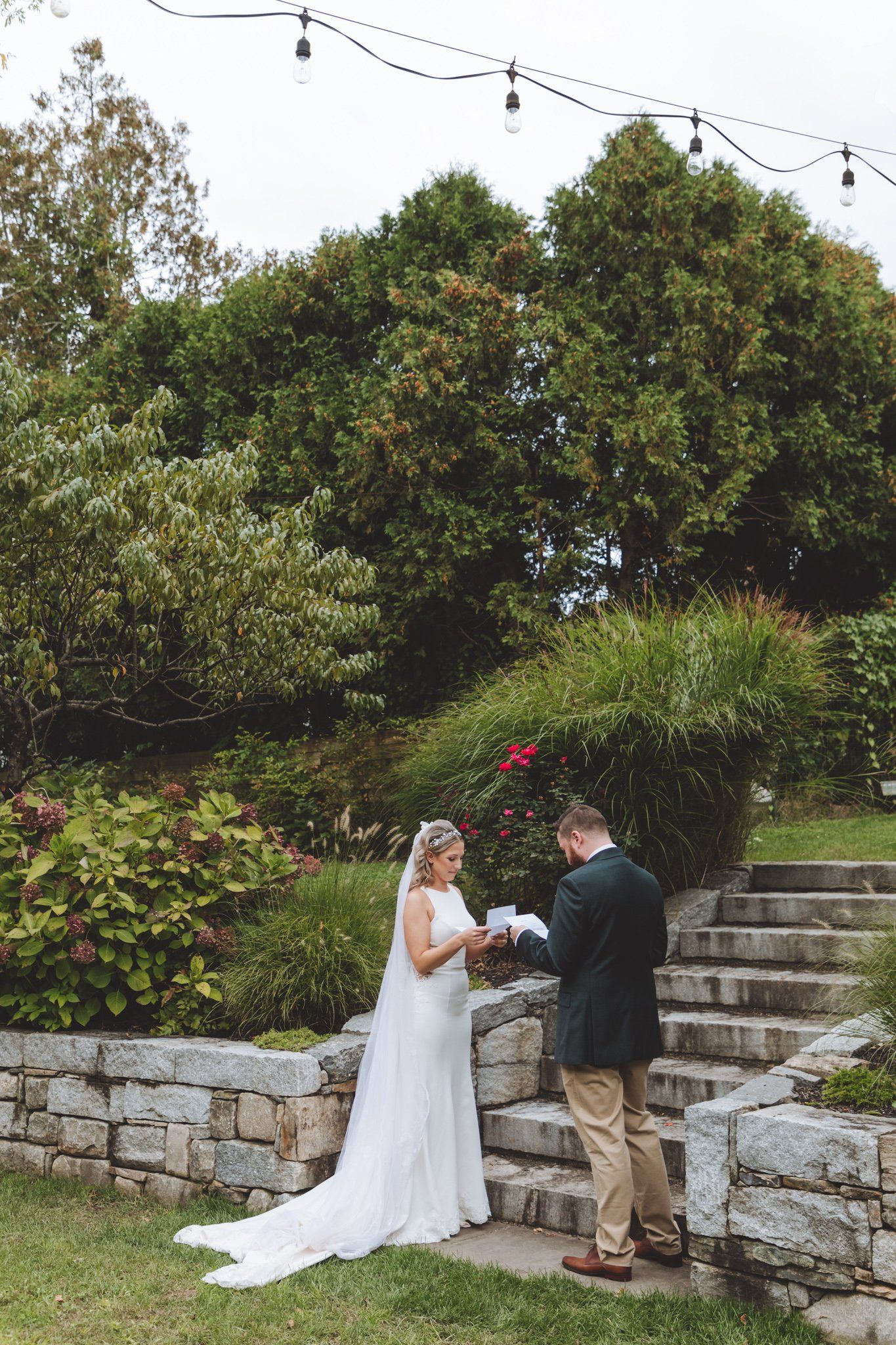 Bride and groom exchanging vows on stone steps in a garden with lush greenery and flowers