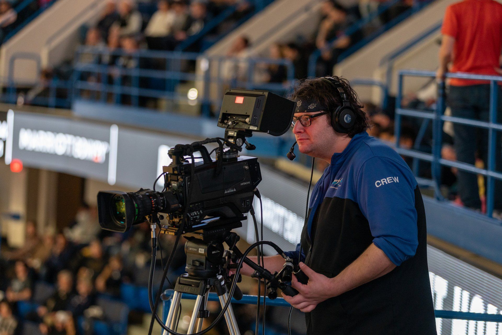 Camera operator filming an indoor sports event from a tripod in a stadium