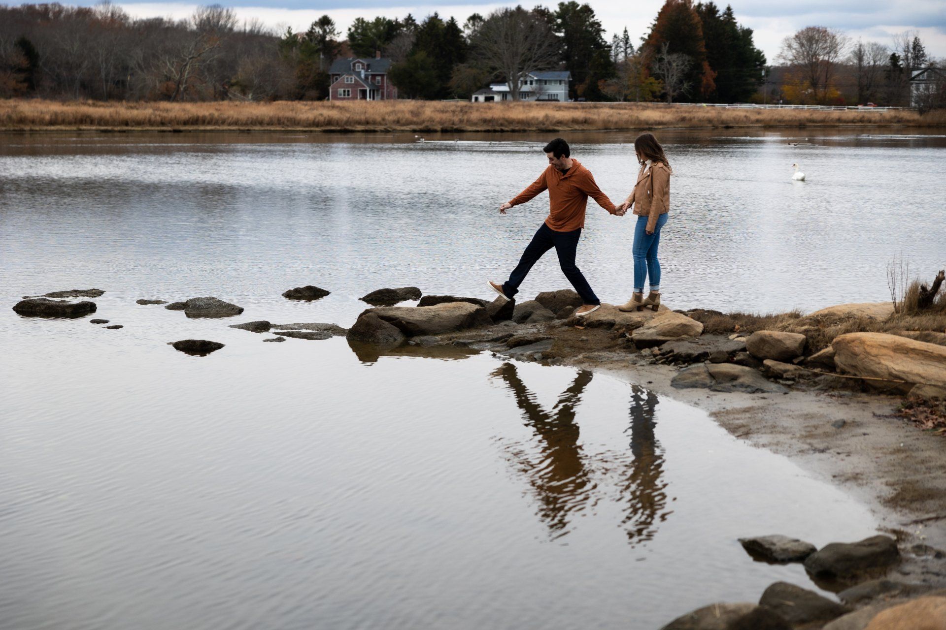 Two people holding hands across stepping stones in a calm lake, with their reflections visible.