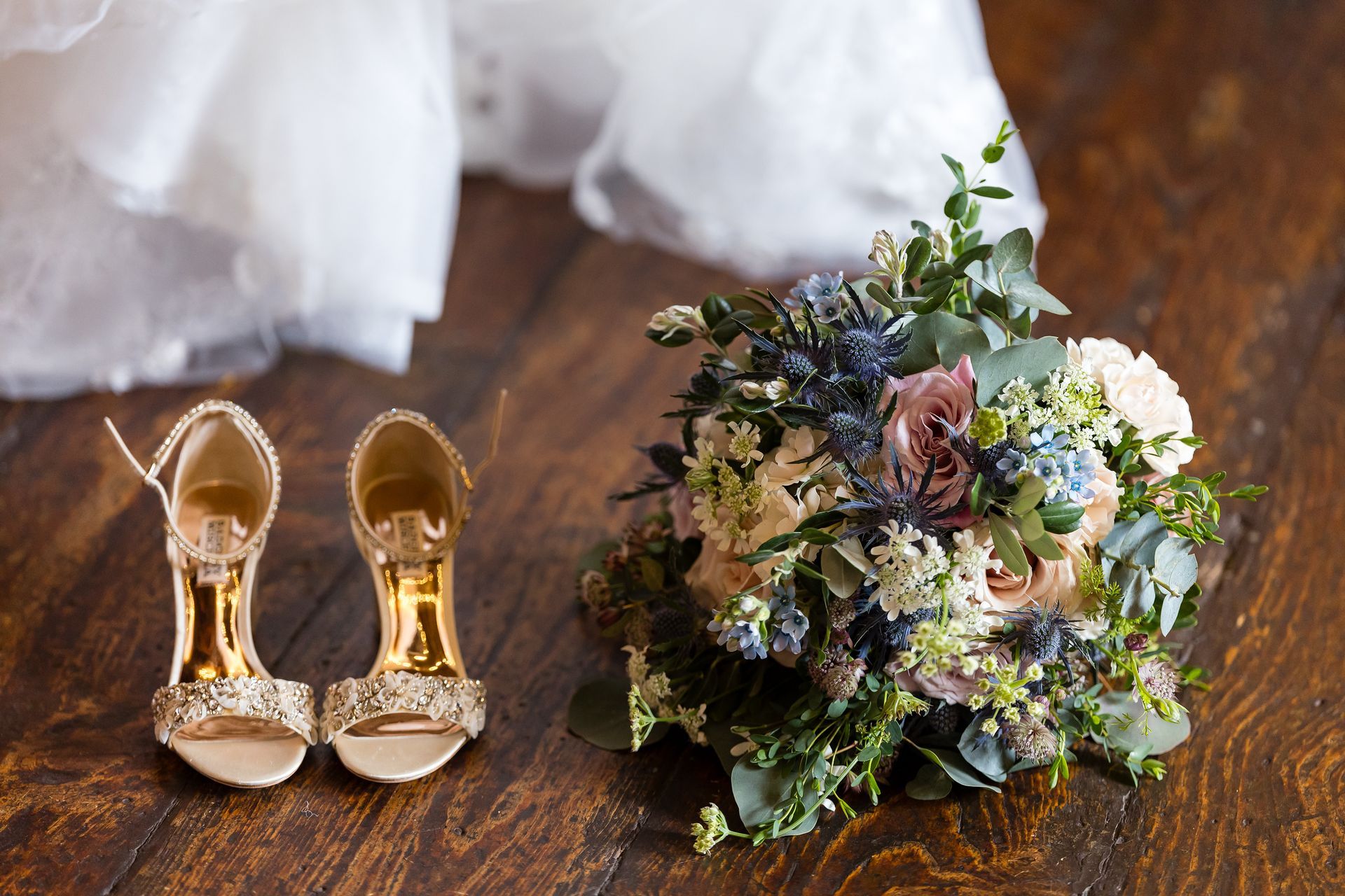 Gold heels beside a colorful bridal bouquet on a wooden floor