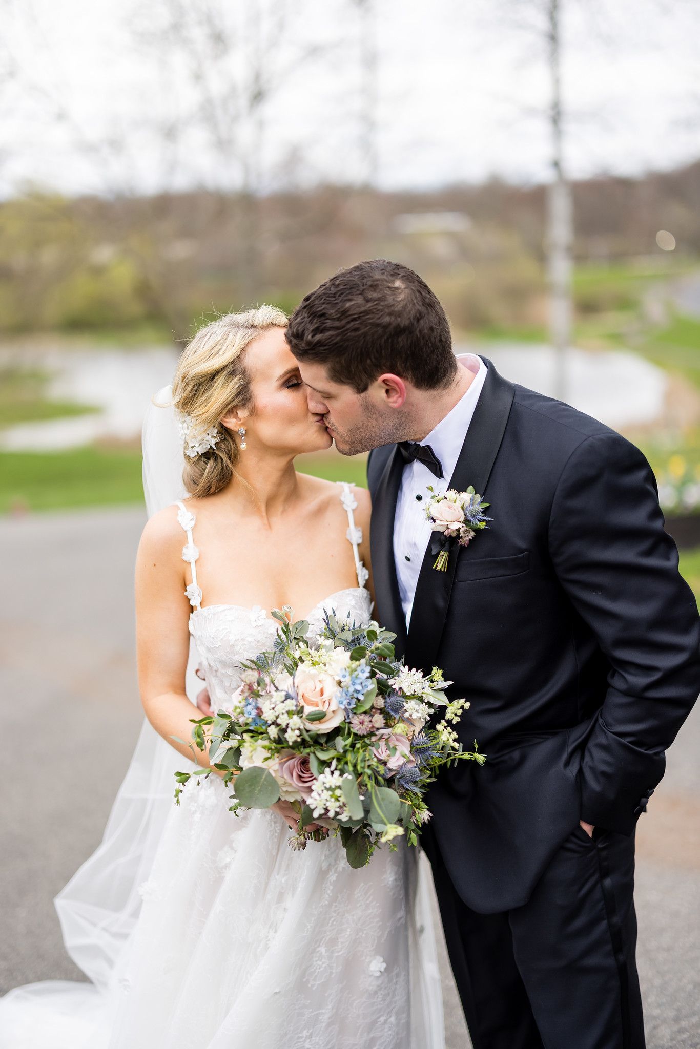 Bride and groom kissing outdoors, bride holding a bouquet in a white gown and groom in a dark suit