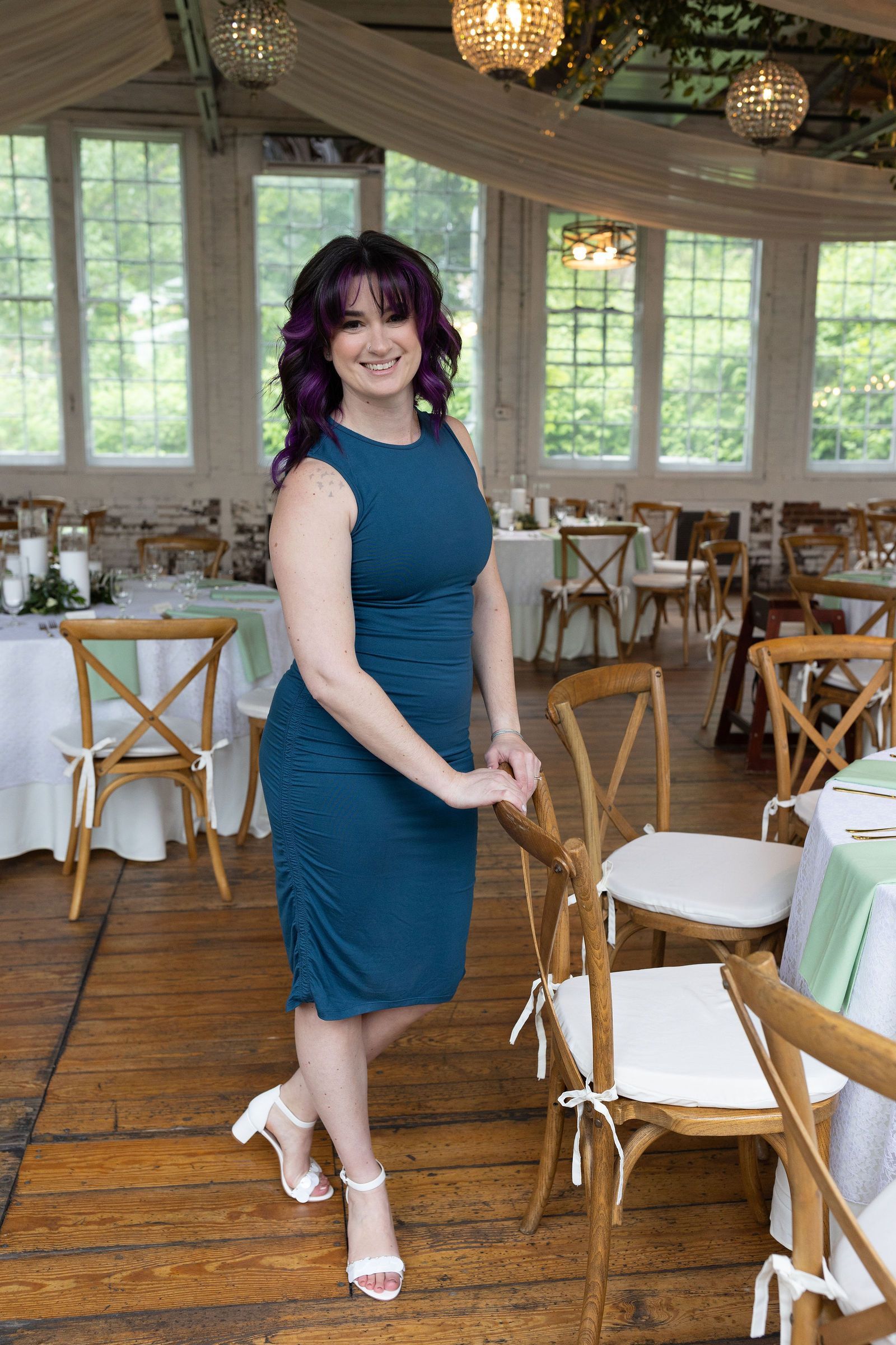 Woman in teal dress and white heels standing in a decorated sunlit event venue