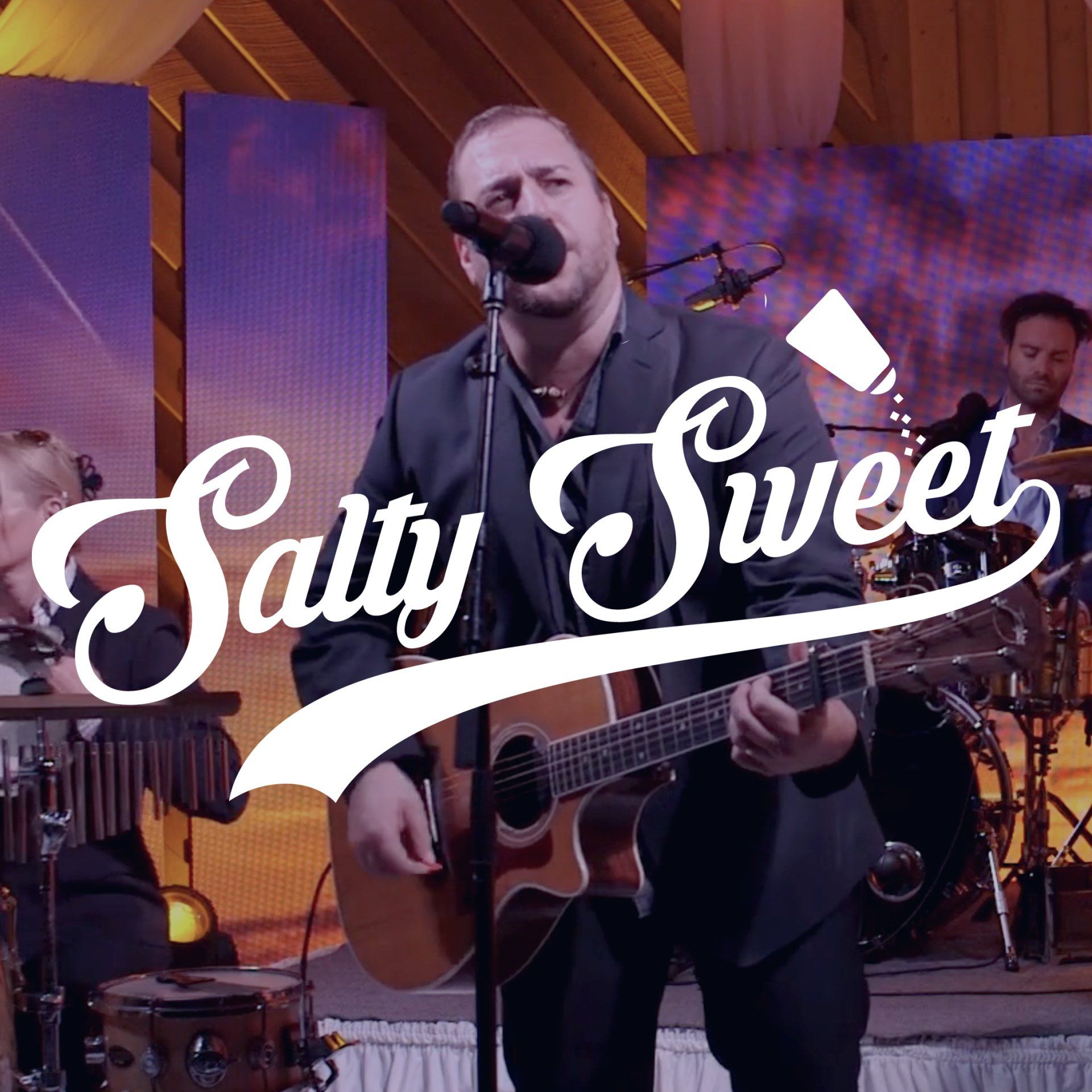 Saly Sweet performing live on stage with guitar and drum set under warm purple lighting