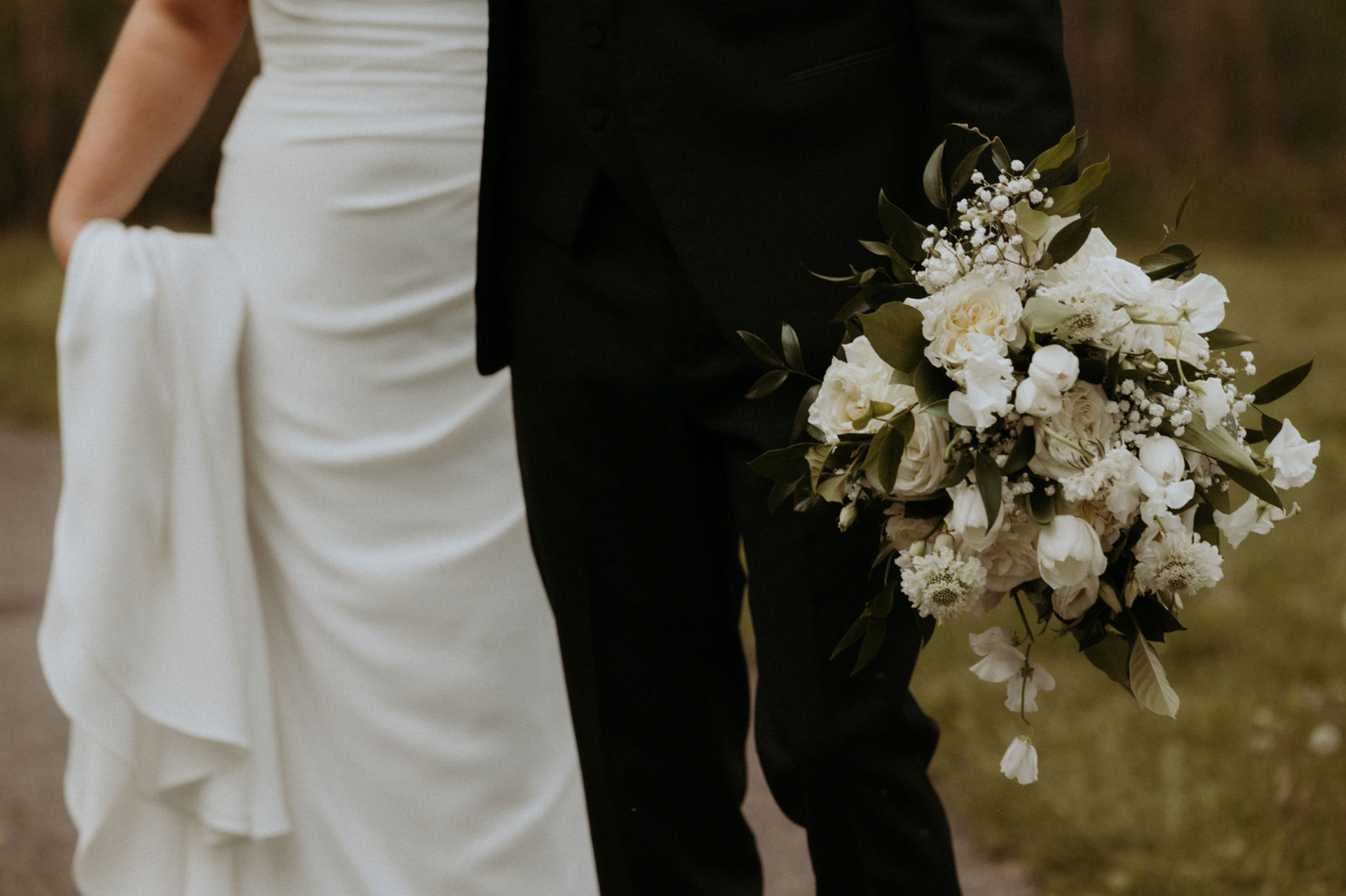 Bride and groom walking outdoors, holding a white floral bouquet