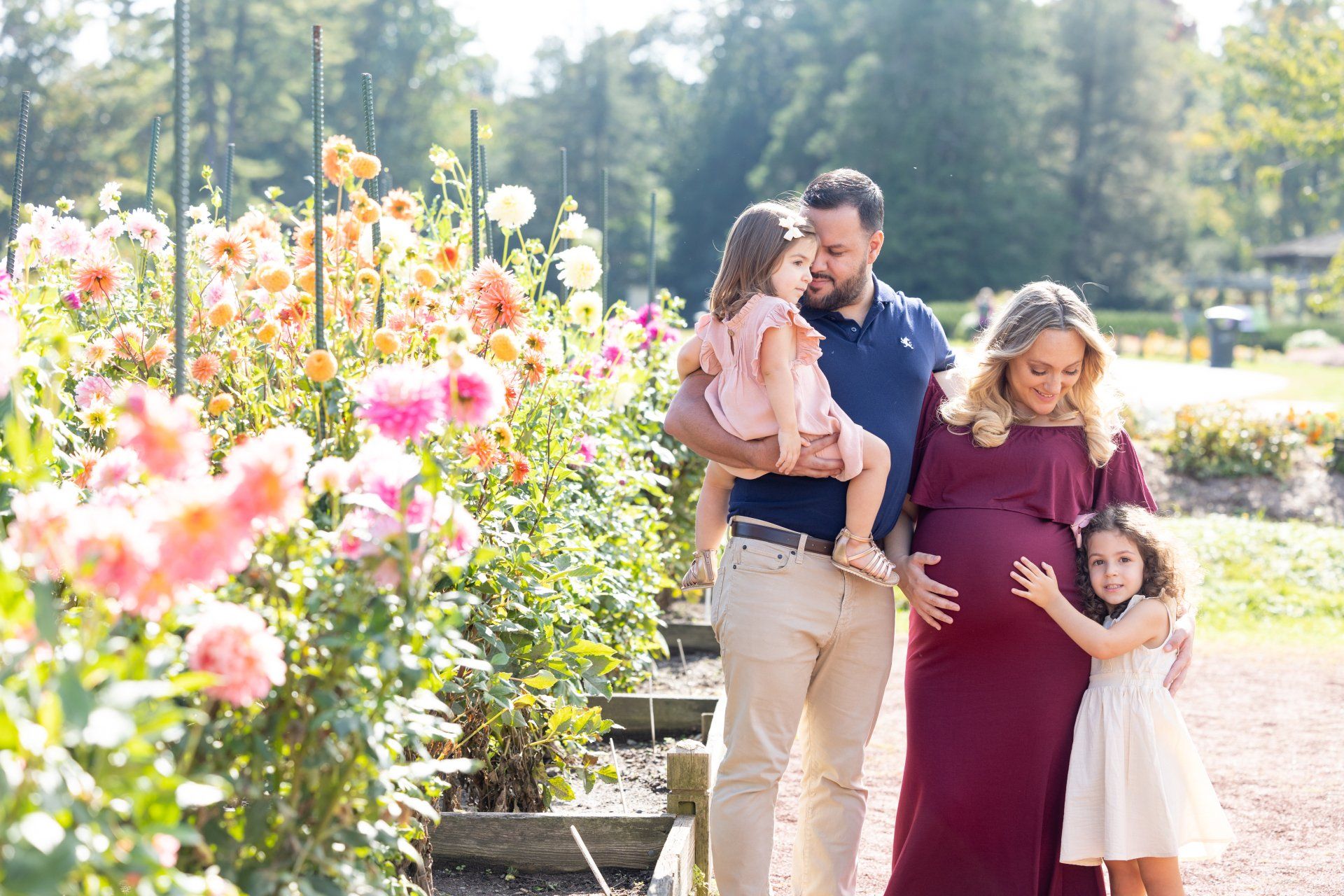 Family of four walking through a sunlit flower garden with colorful blooms.