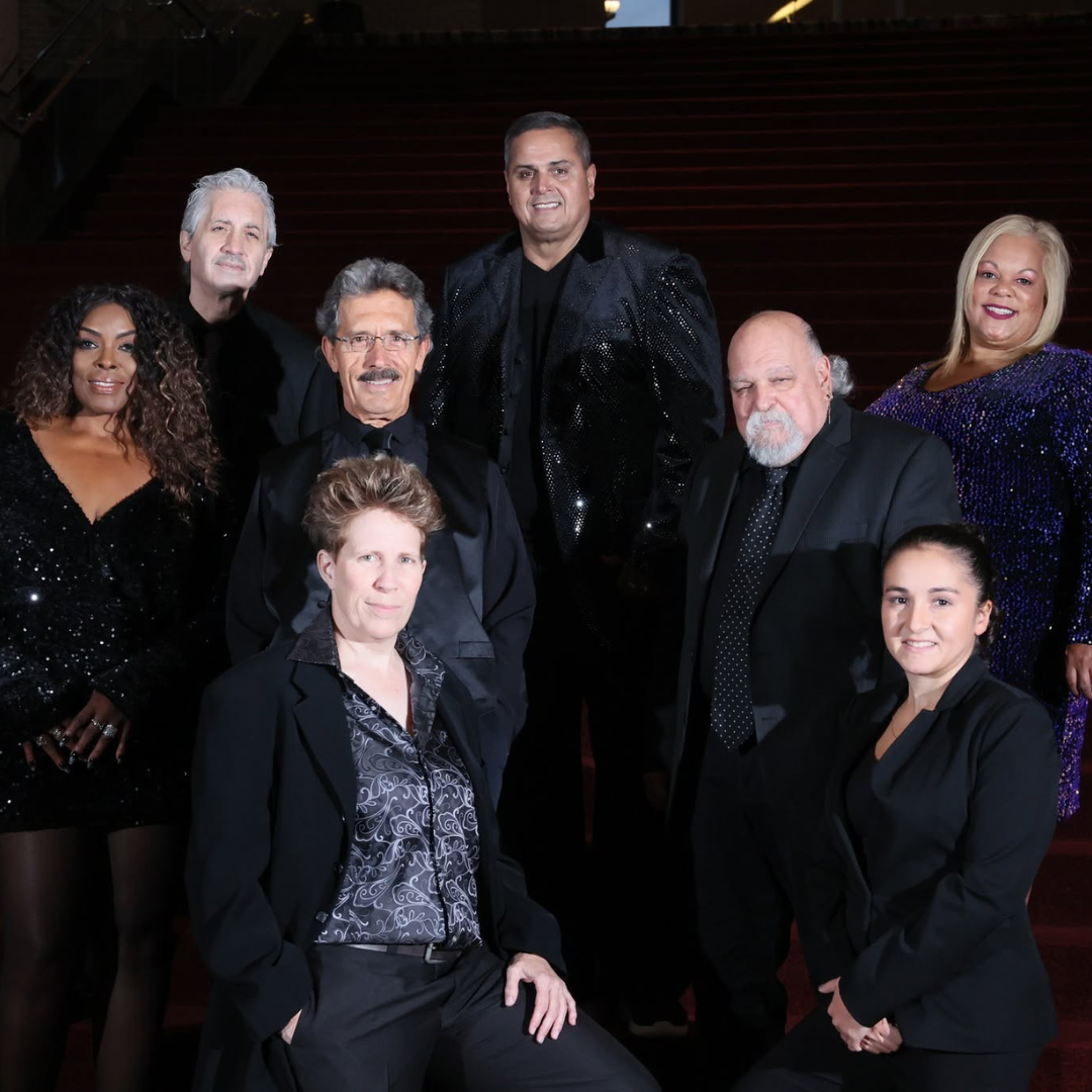Seven people posing in dark formal attire on a dimly lit staircase at an evening event