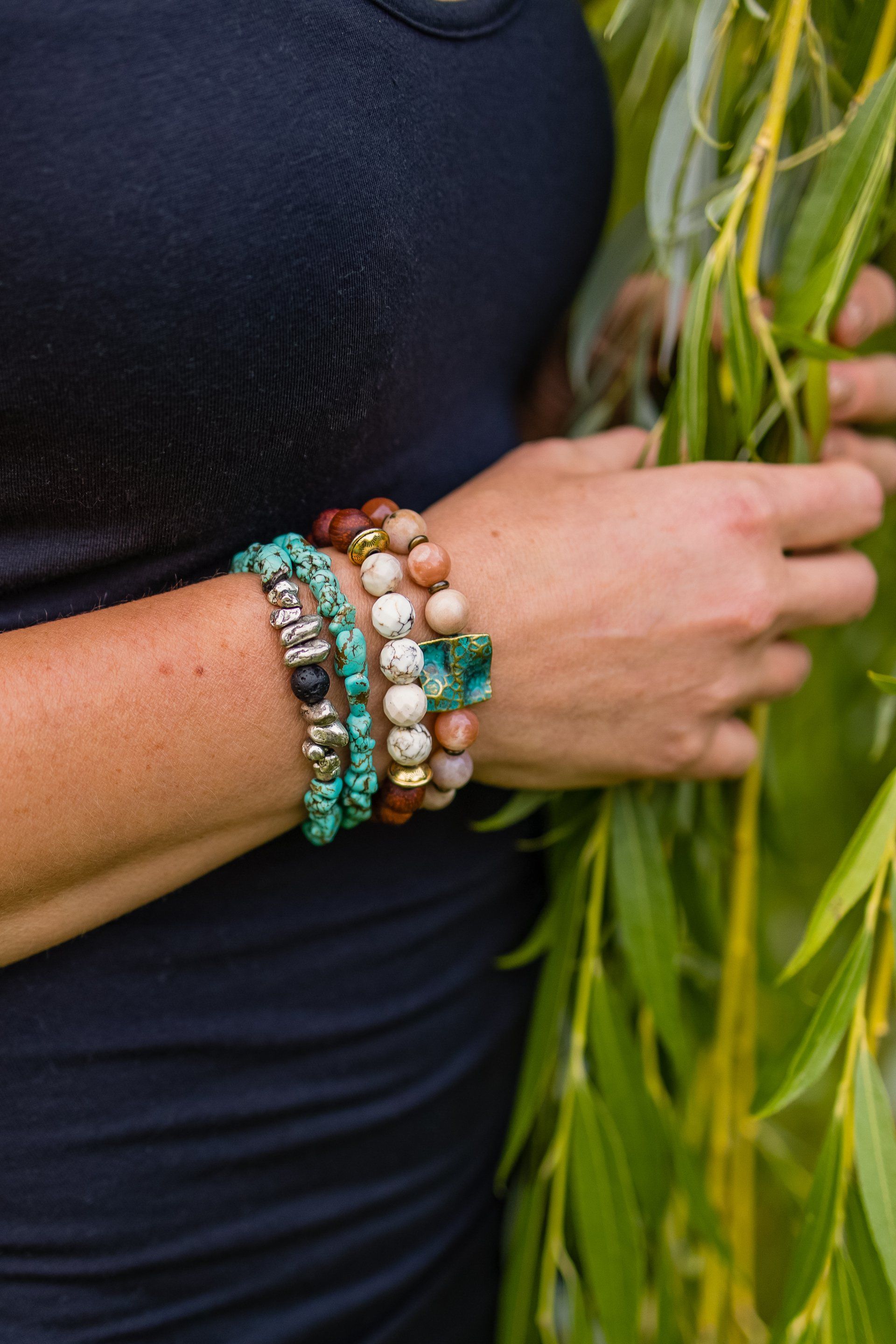 Hand wearing stacked turquoise, white, and silver bracelets beside green leaves