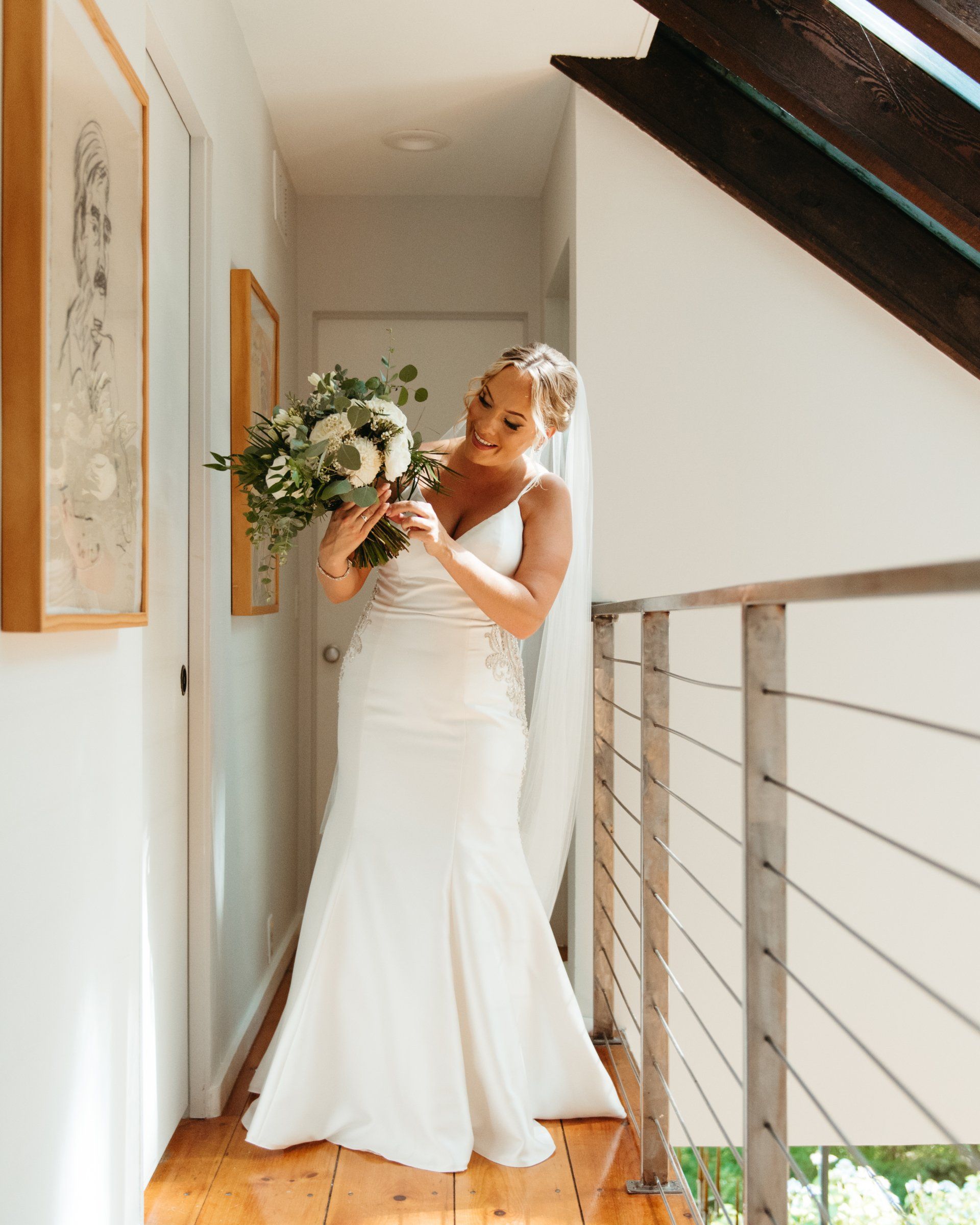 Bride in a white gown holding a bouquet in a bright stairwell.